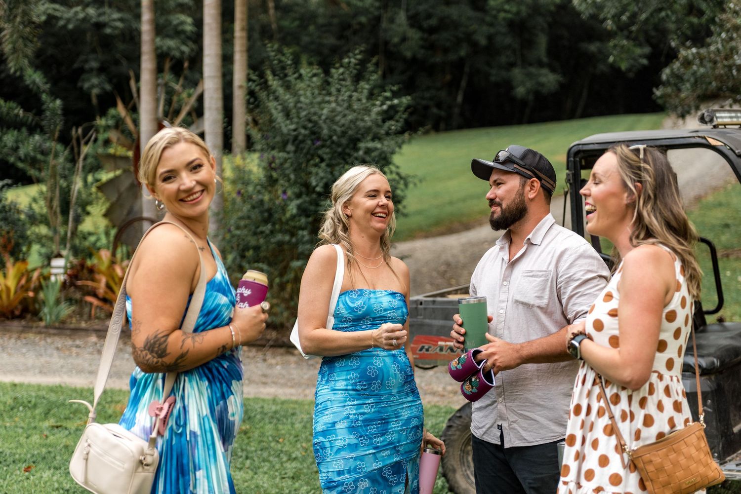 Two blonde women and friends laughing together outdoors at casual garden party event.