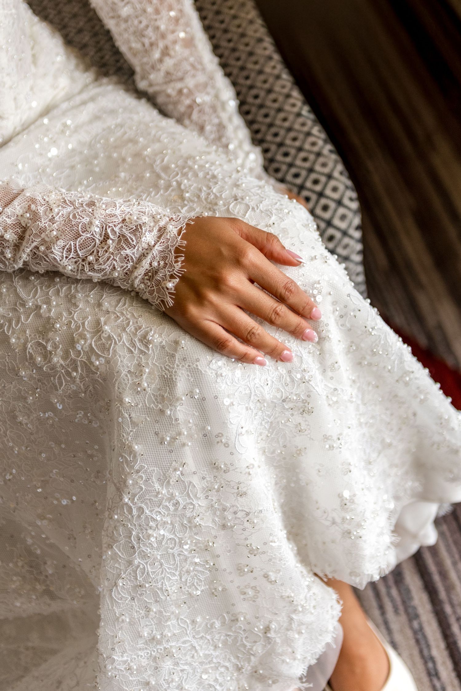 Close-up of bride's hand resting on intricate white beaded lace wedding dress fabric.