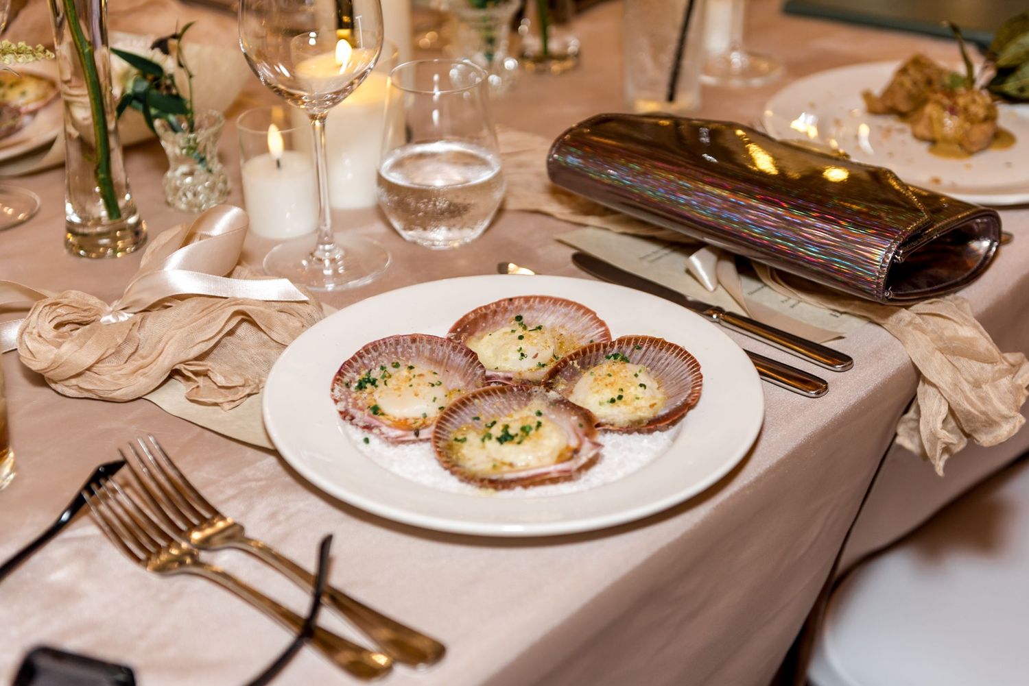 Elegant wedding reception starter dish of scallops served on white plate with gold cutlery.