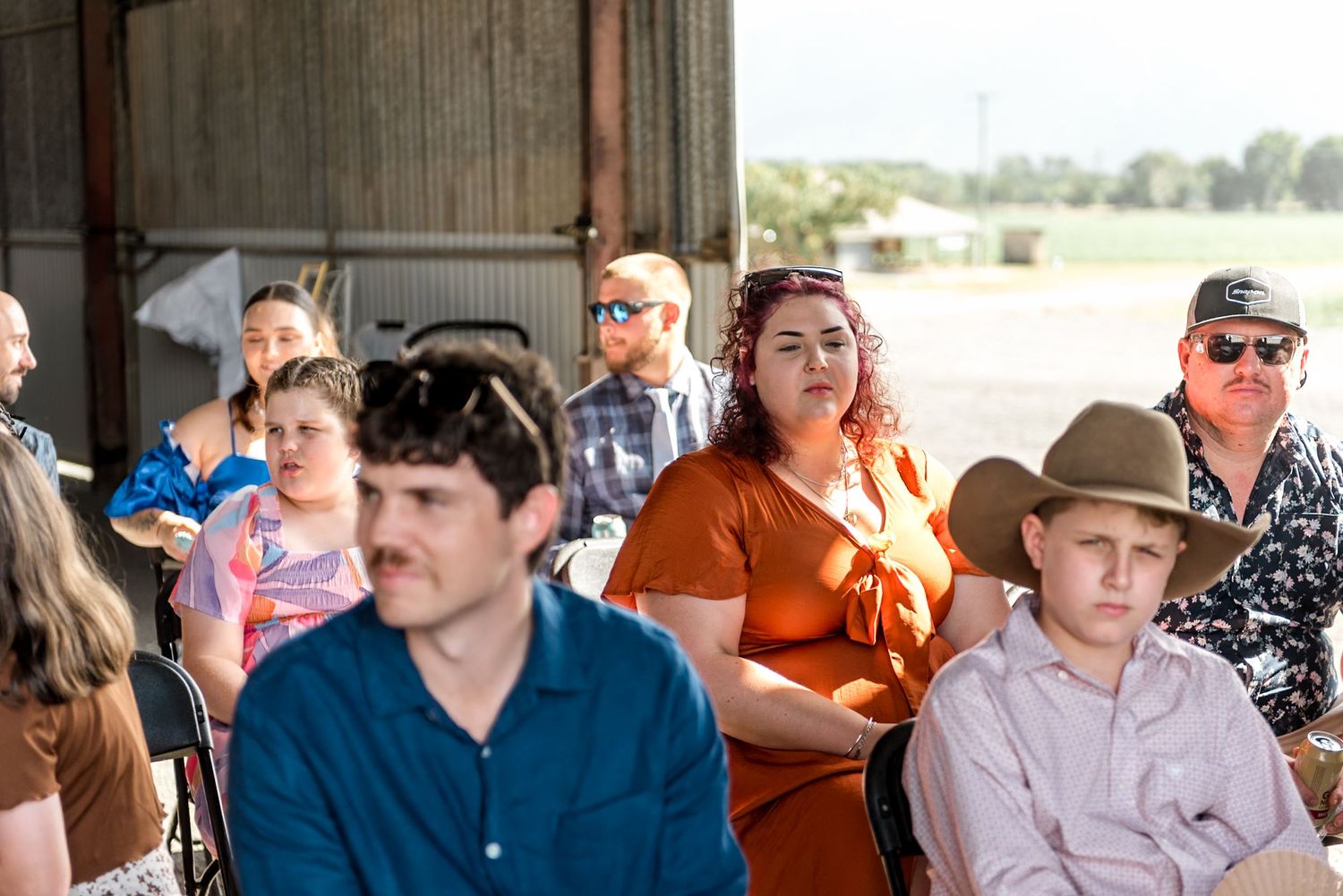 Wedding guests seated in a barn venue, including a woman in orange and a boy in a cowboy hat.