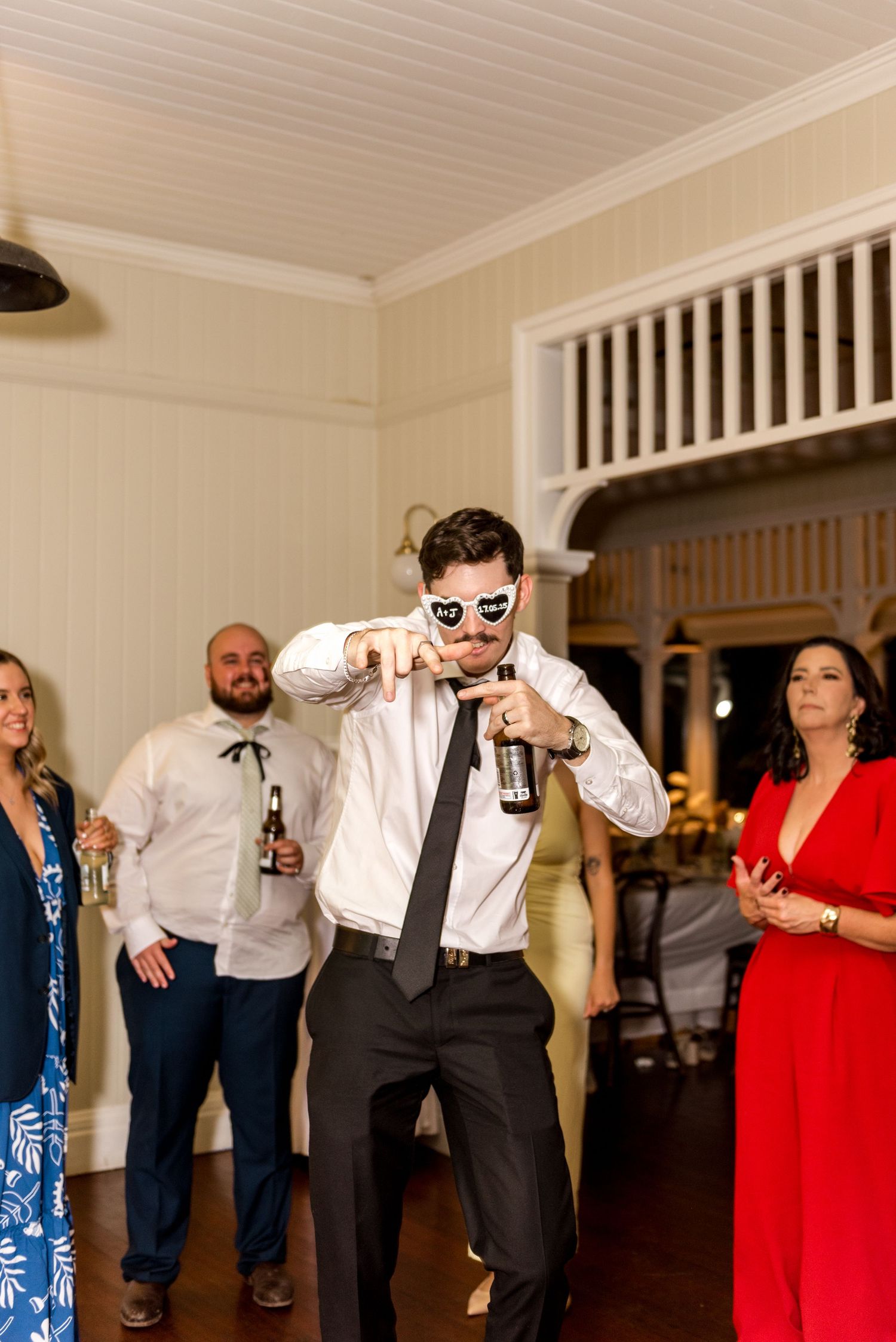 Guest in black tie and novelty sunglasses dancing energetically at a wedding reception.