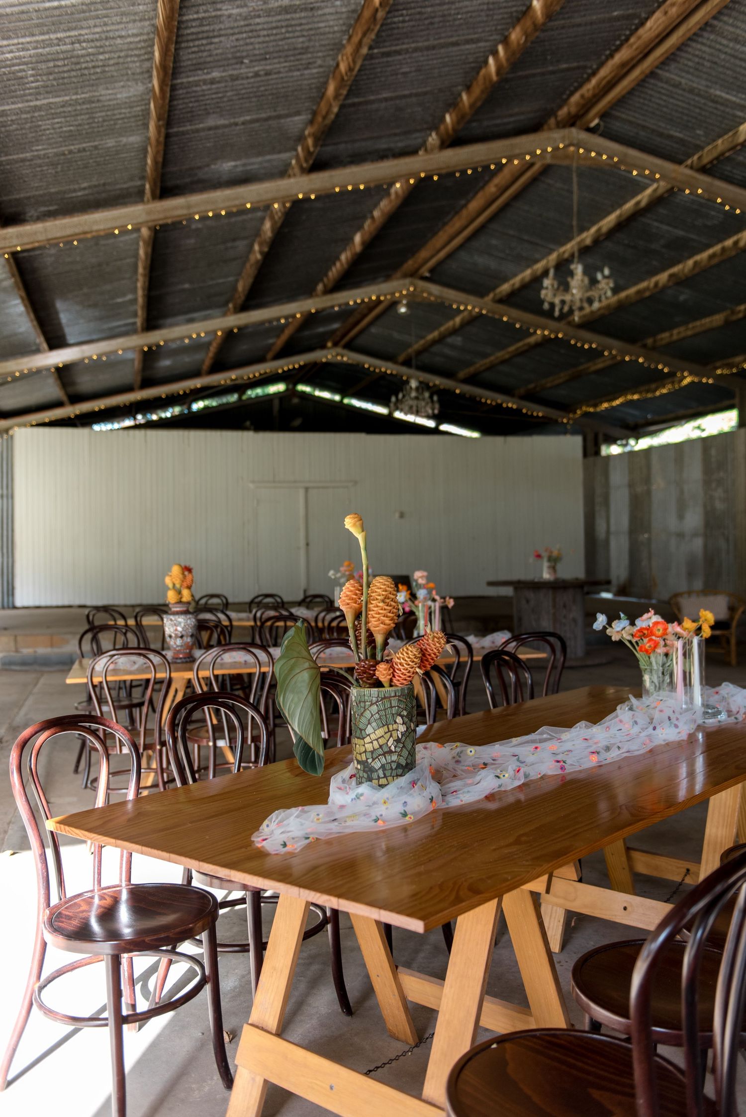Rustic barn wedding reception venue with wooden tables, bentwood chairs, fairy lights and tropical centerpieces.