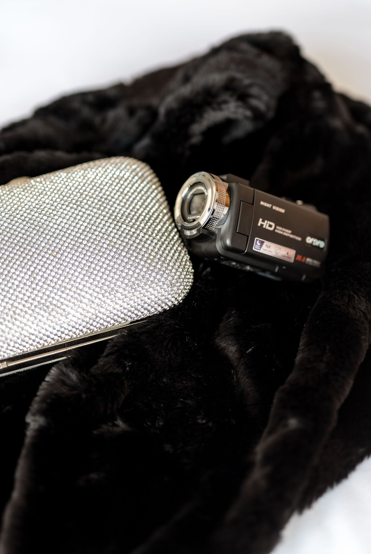 Sony HD camcorder and silver rhinestone clutch purse resting on black faux fur for wedding day.