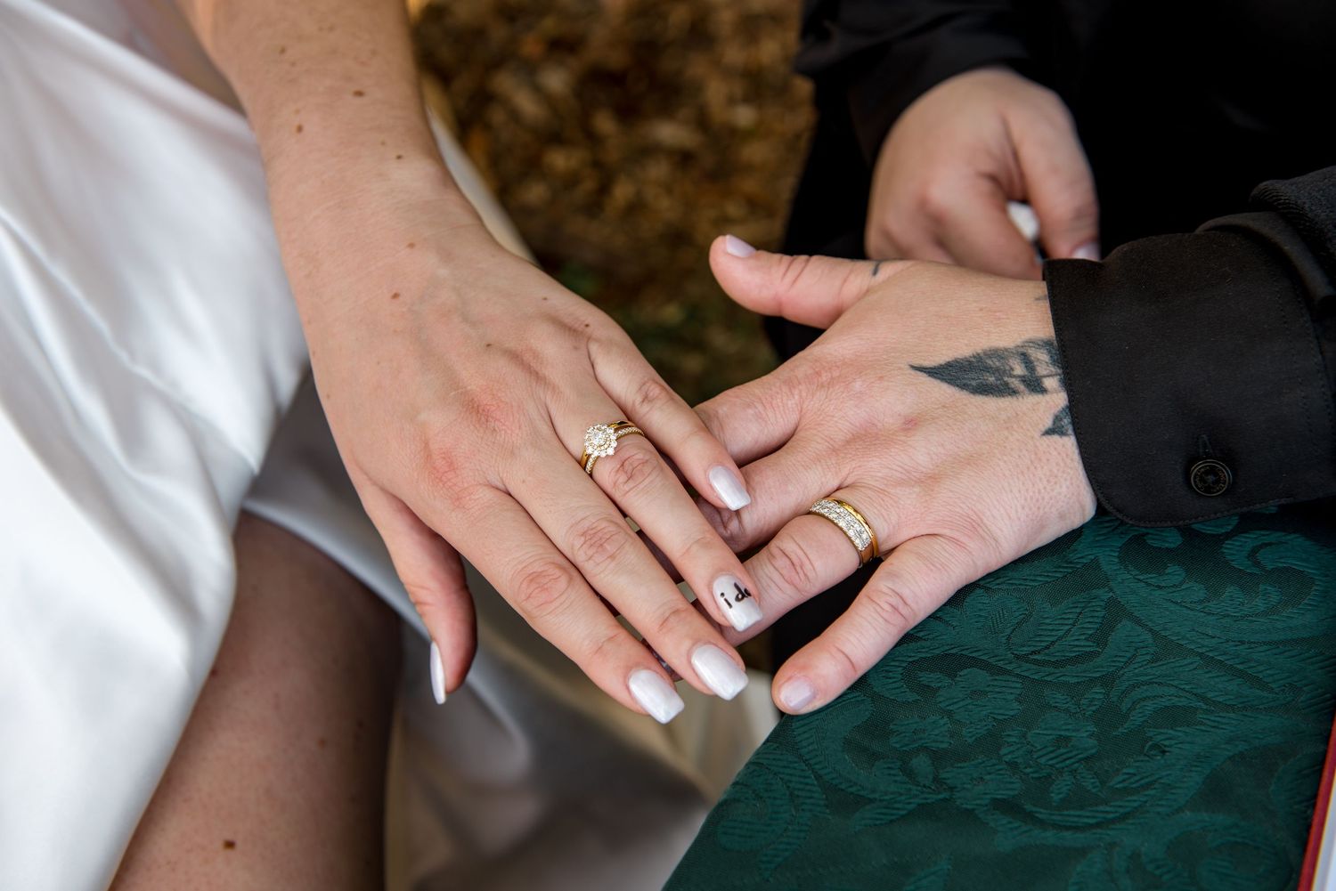 Close-up of newlyweds displaying matching gold wedding rings with tattooed hands.