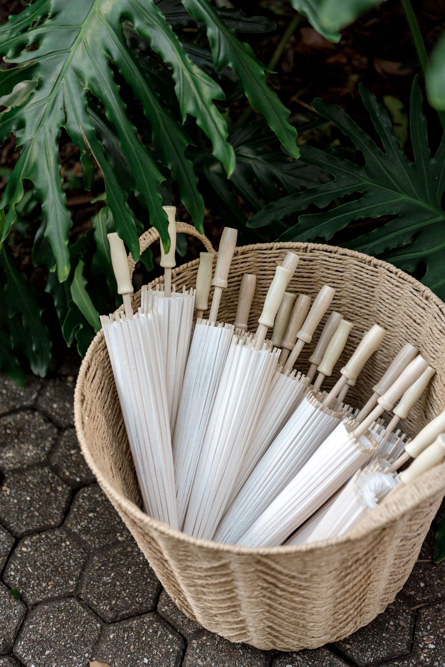 White parasols arranged in a wicker basket for outdoor wedding ceremony guests.
