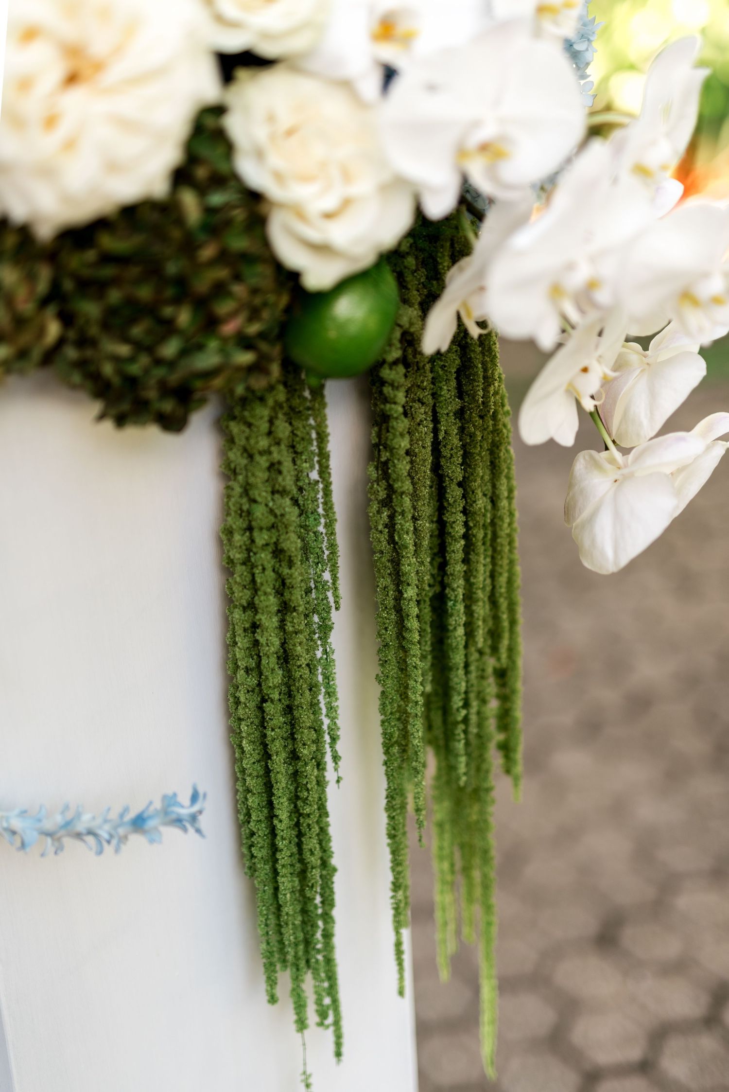 White wedding pillar decorated with cascading green amaranthus, white orchids, roses, and lime accents.