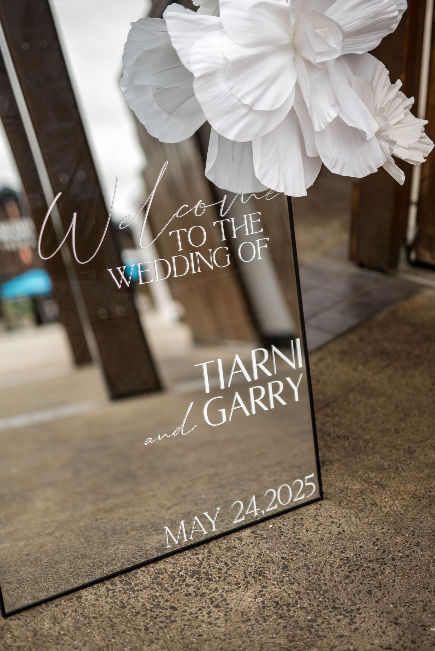 Elegant mirrored wedding welcome sign for Tiarni and Garry's May 24 2025 wedding decorated with white flowers.