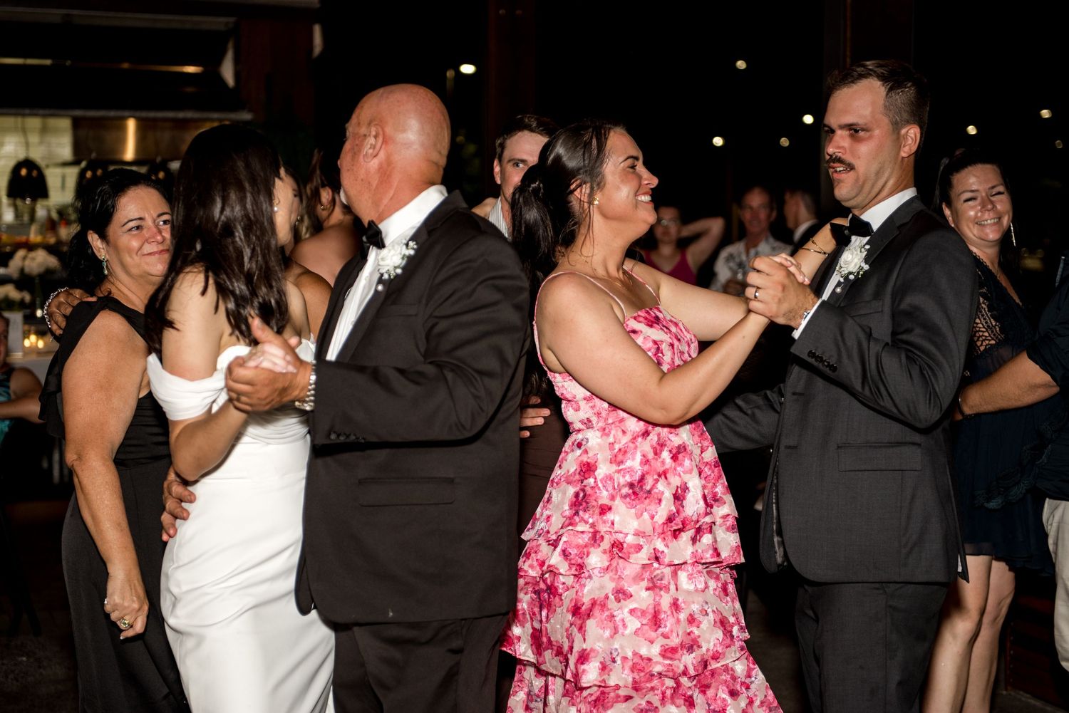 Bride and groom share parent dances simultaneously with guests celebrating on the wedding dance floor.