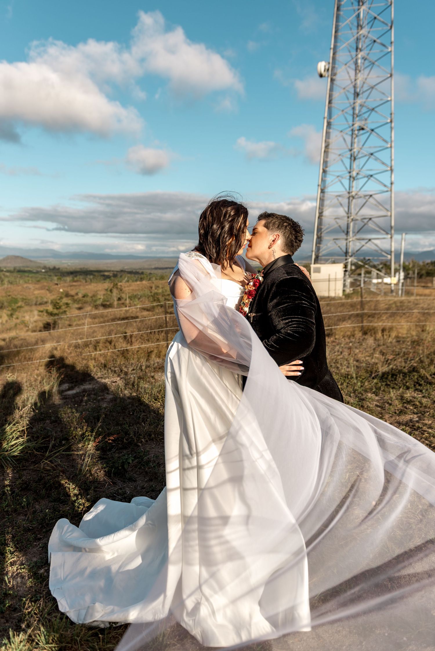 Bride and groom kissing outdoors with veil flowing in the wind on their wedding day.