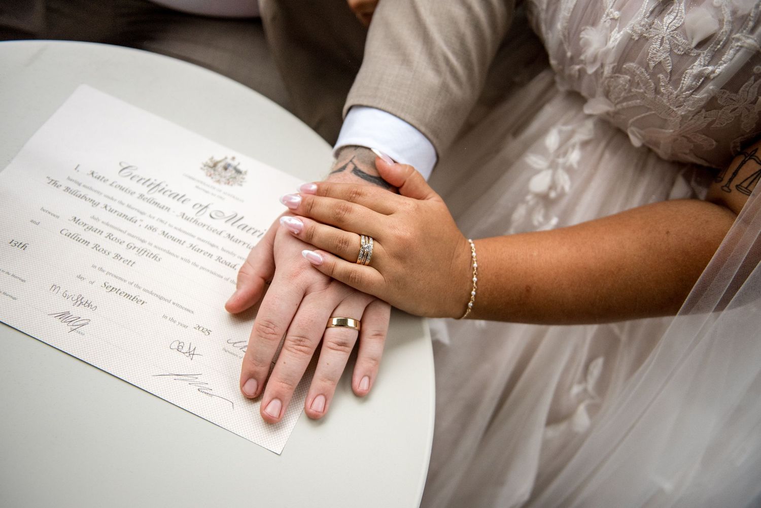 Newlyweds hands with wedding rings resting on Australian Certificate of Marriage after signing ceremony.