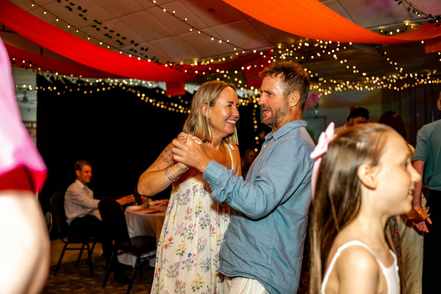 Couple shares a joyful dance at a wedding reception while a young girl watches nearby.