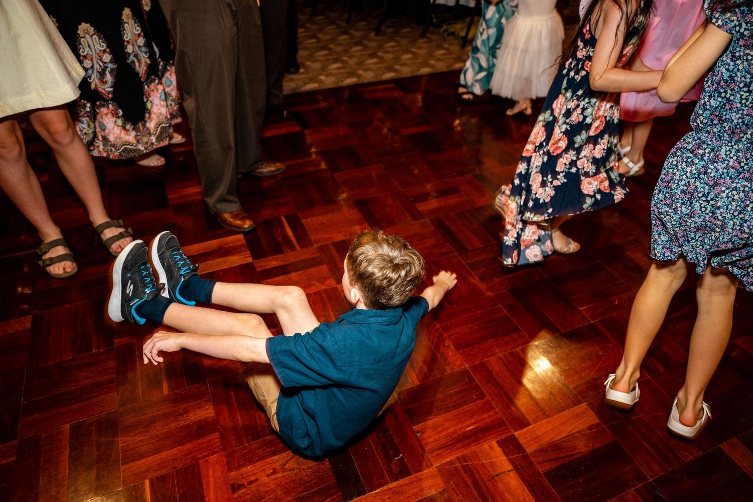 Young child sitting on wooden dance floor at a lively wedding reception.
