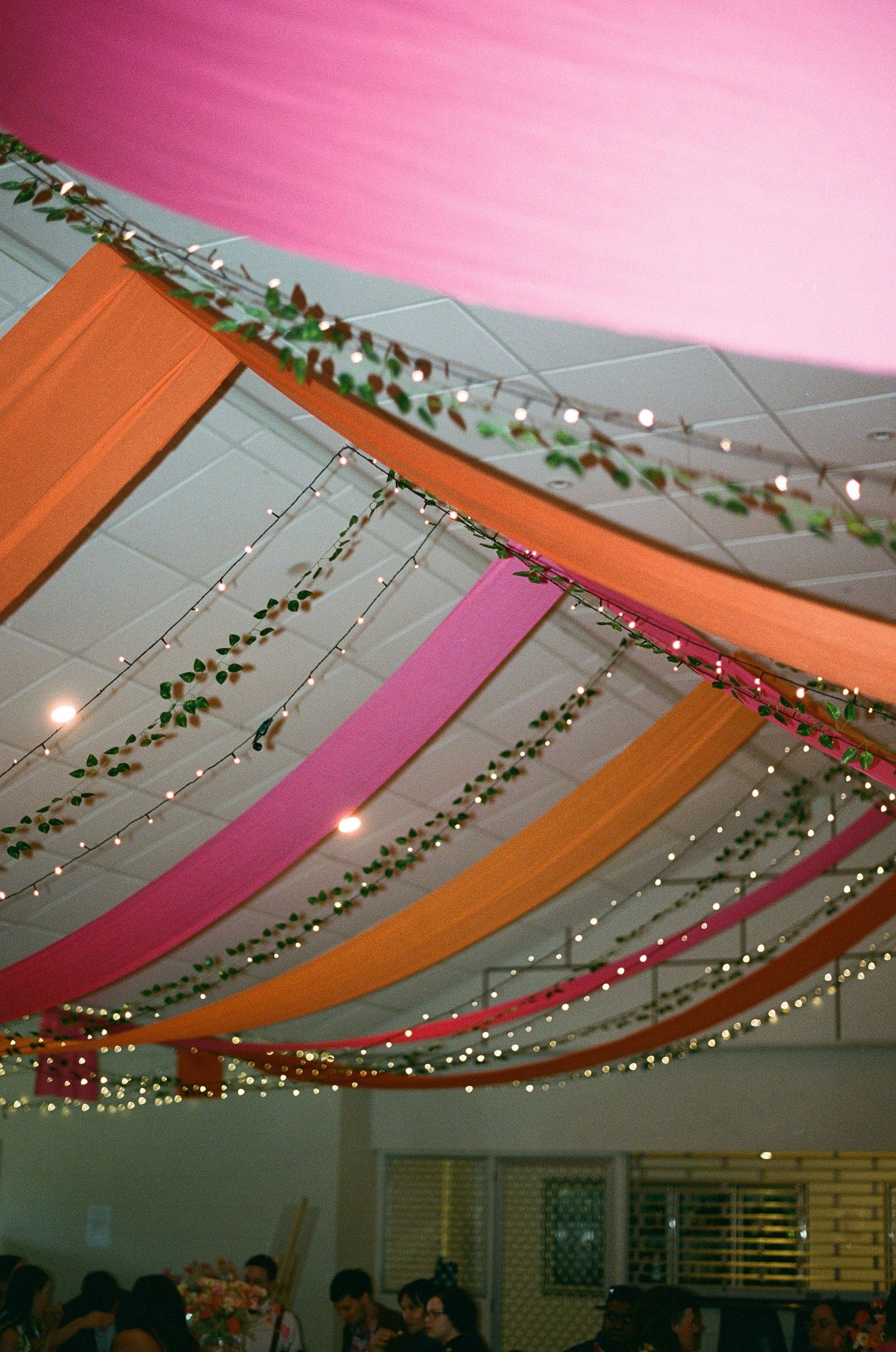 Vibrant pink and orange fabric draping with fairy lights decorating wedding venue ceiling.
