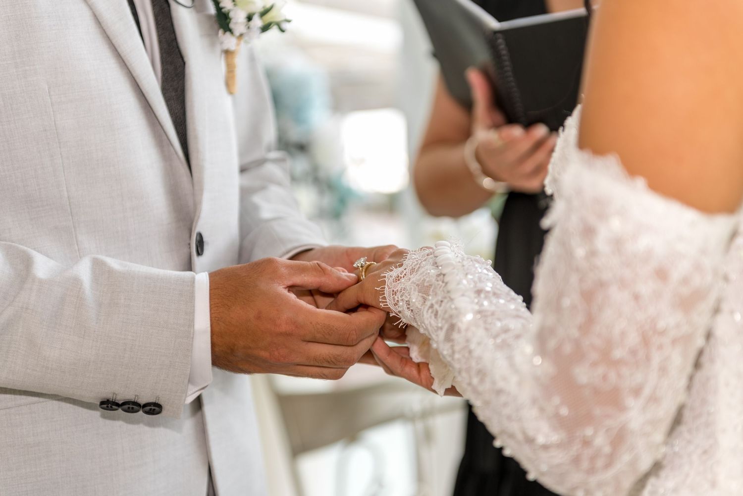 Close-up of groom placing wedding ring on bride's finger during ring exchange ceremony.