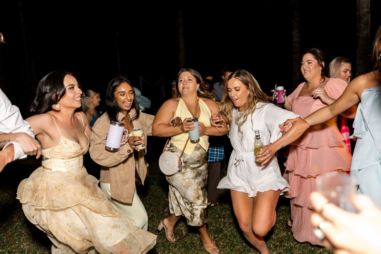 Women in elegant dresses dancing and celebrating at outdoor nighttime wedding reception.