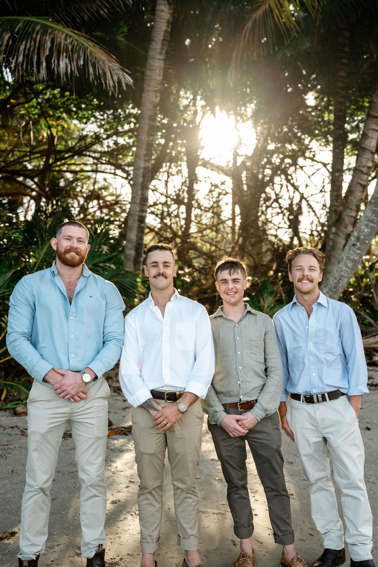 Four groomsmen in casual linen shirts and khaki pants posing on a tropical beach at golden hour at Four Mile Beach, Port Douglas.