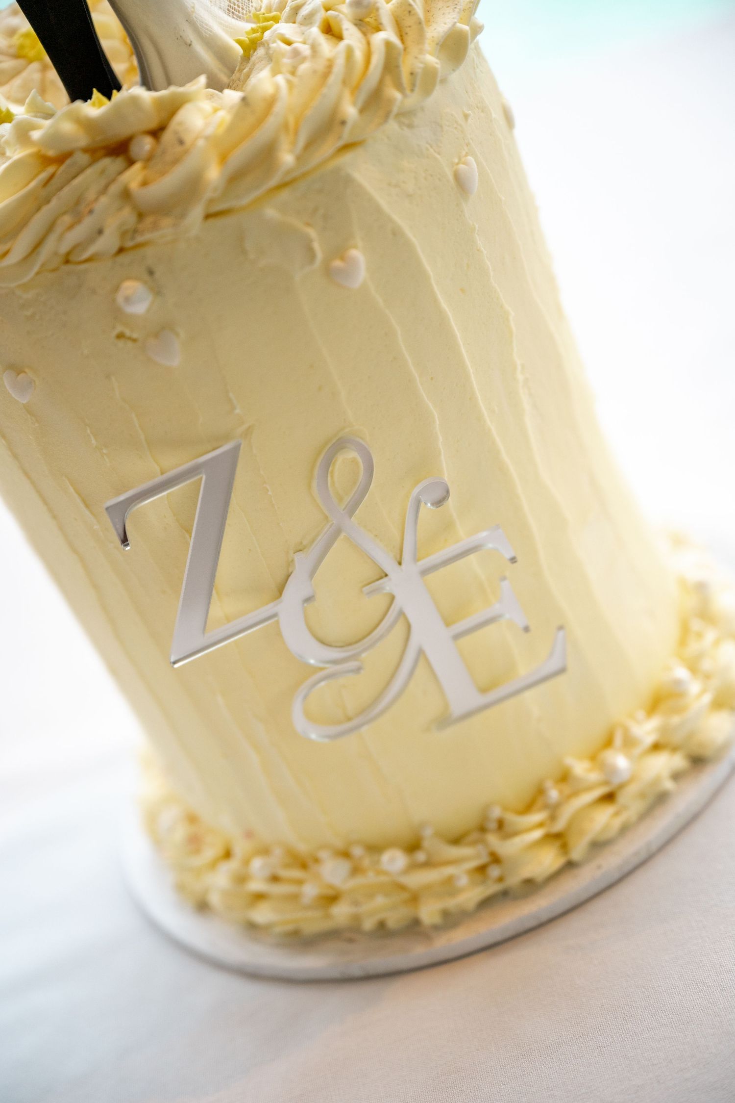 Close-up of white wedding cake with silver Z&E monogram decoration and cream frosting details at Sheraton Grand Mirage Port Douglas.