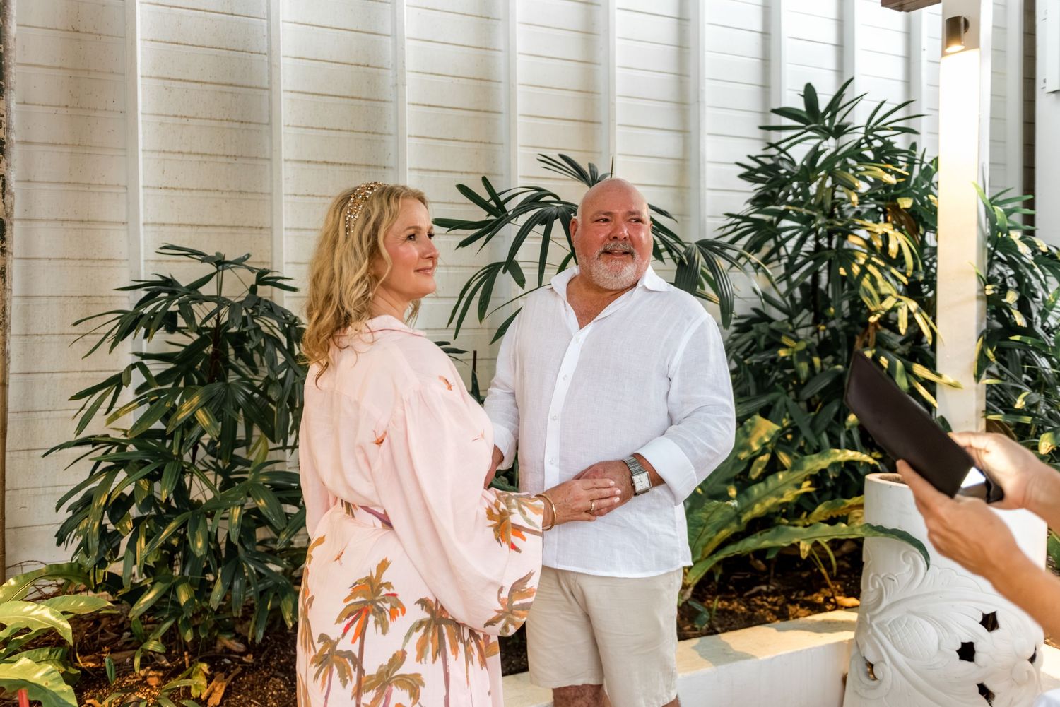 Newlywed couple smiling together after wedding ceremony with tropical garden backdrop.