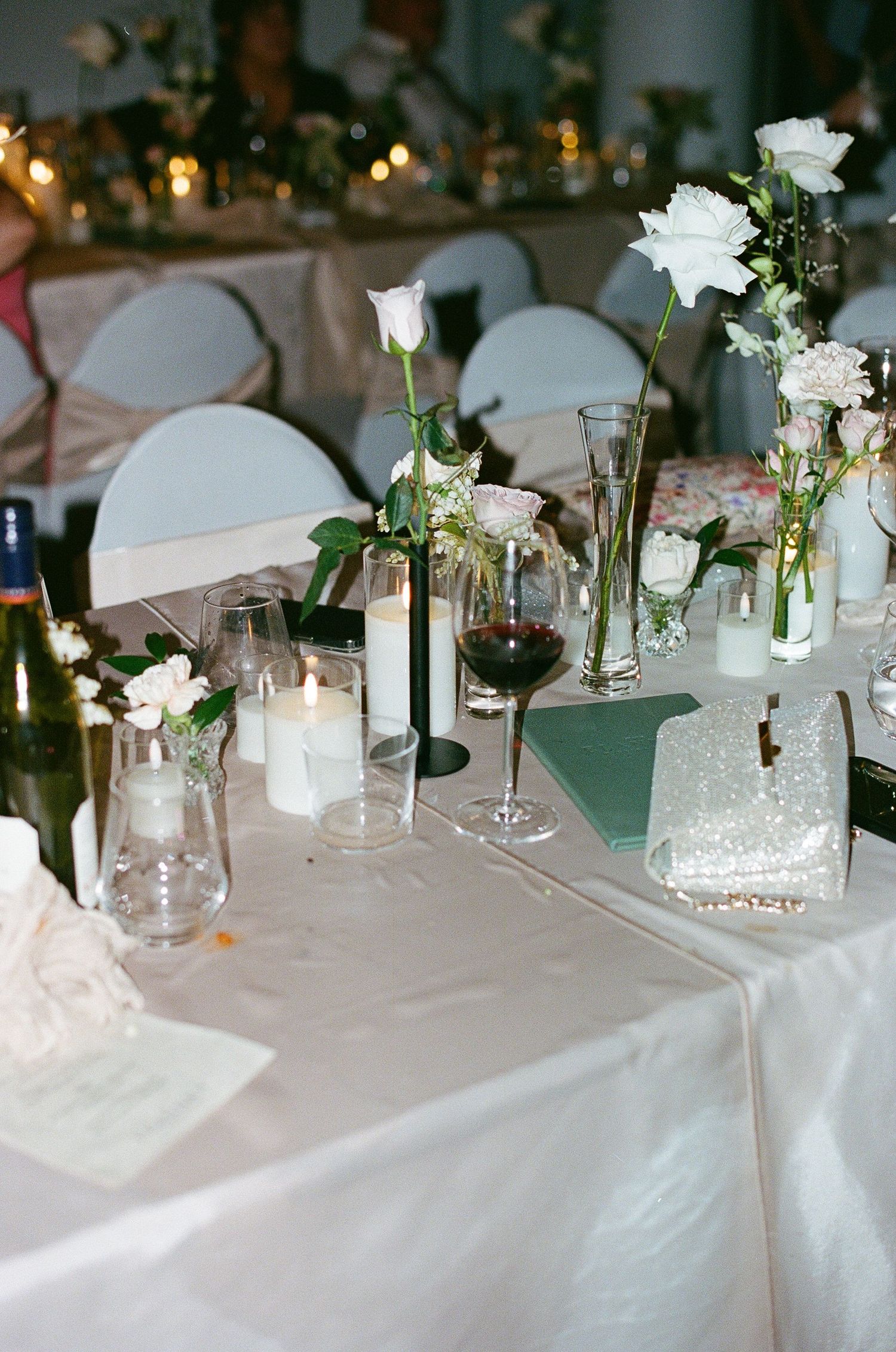 Elegant wedding reception table with white roses, candles, and wine glasses.