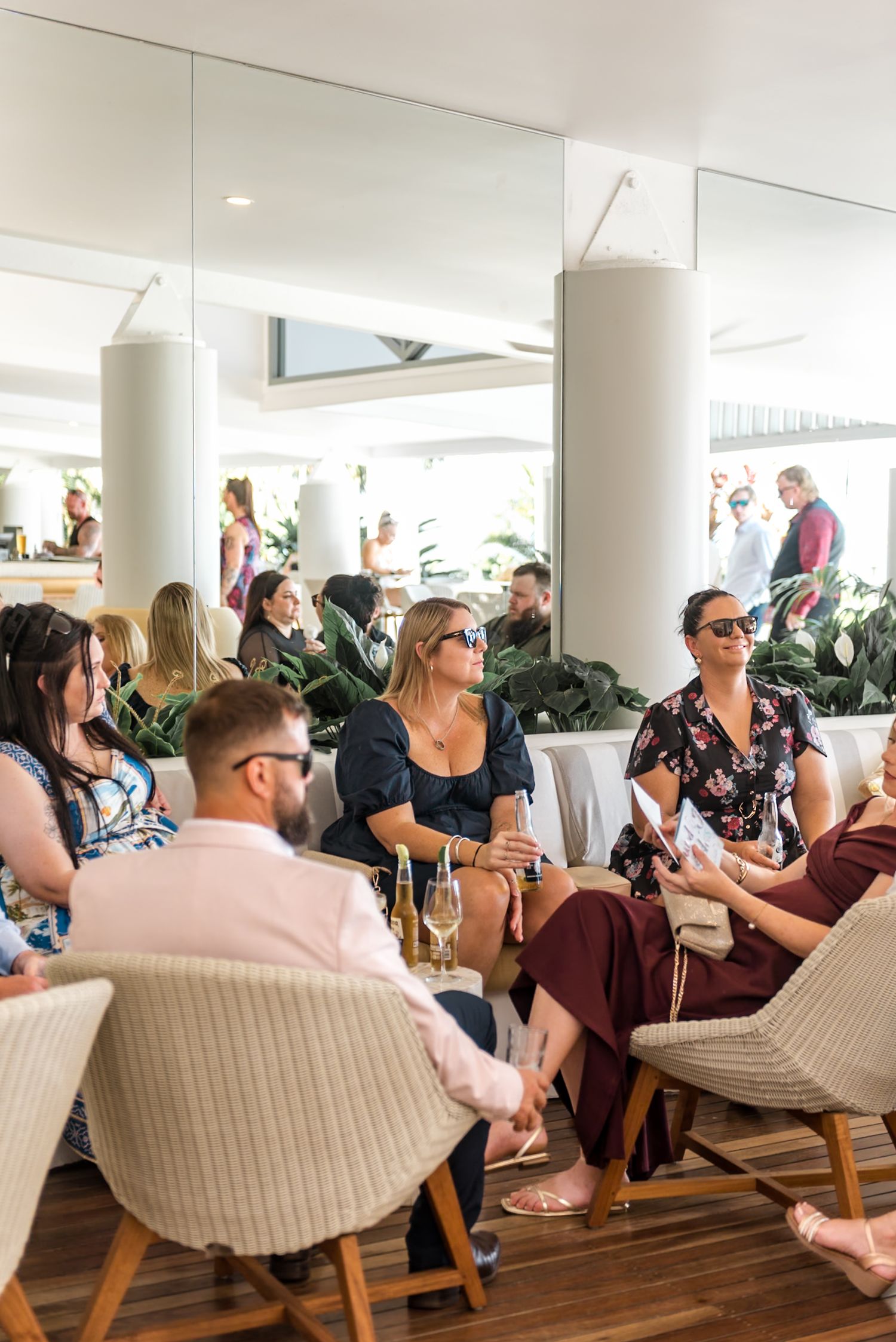 Wedding guests socializing and relaxing in a modern bright venue with white columns and lush indoor tropical plants.