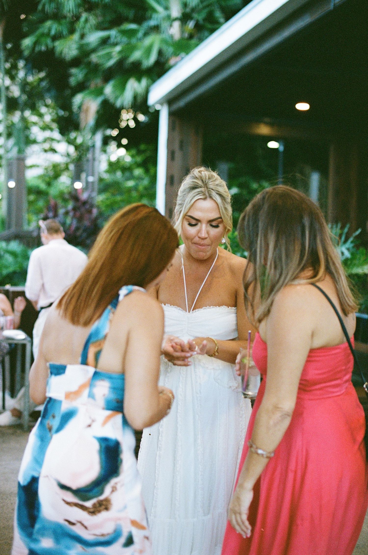 Bride in a white strapless dress surrounded by guests at an outdoor tropical wedding reception.
