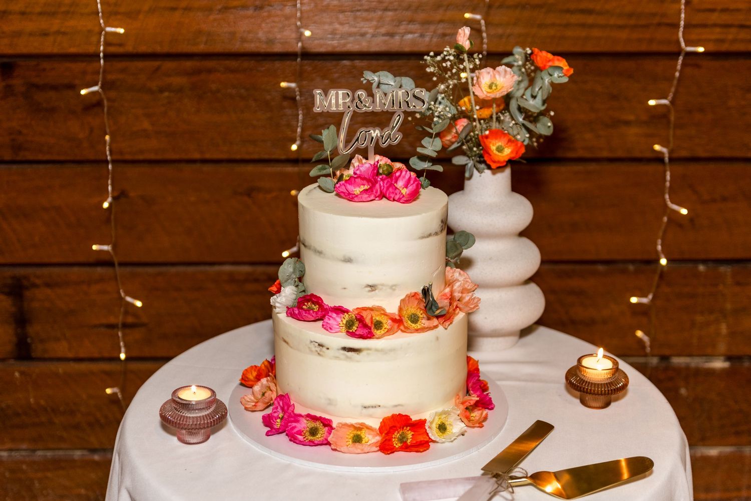 Two-tier naked wedding cake decorated with vibrant pink and orange flowers and a Mr and Mrs cake topper.