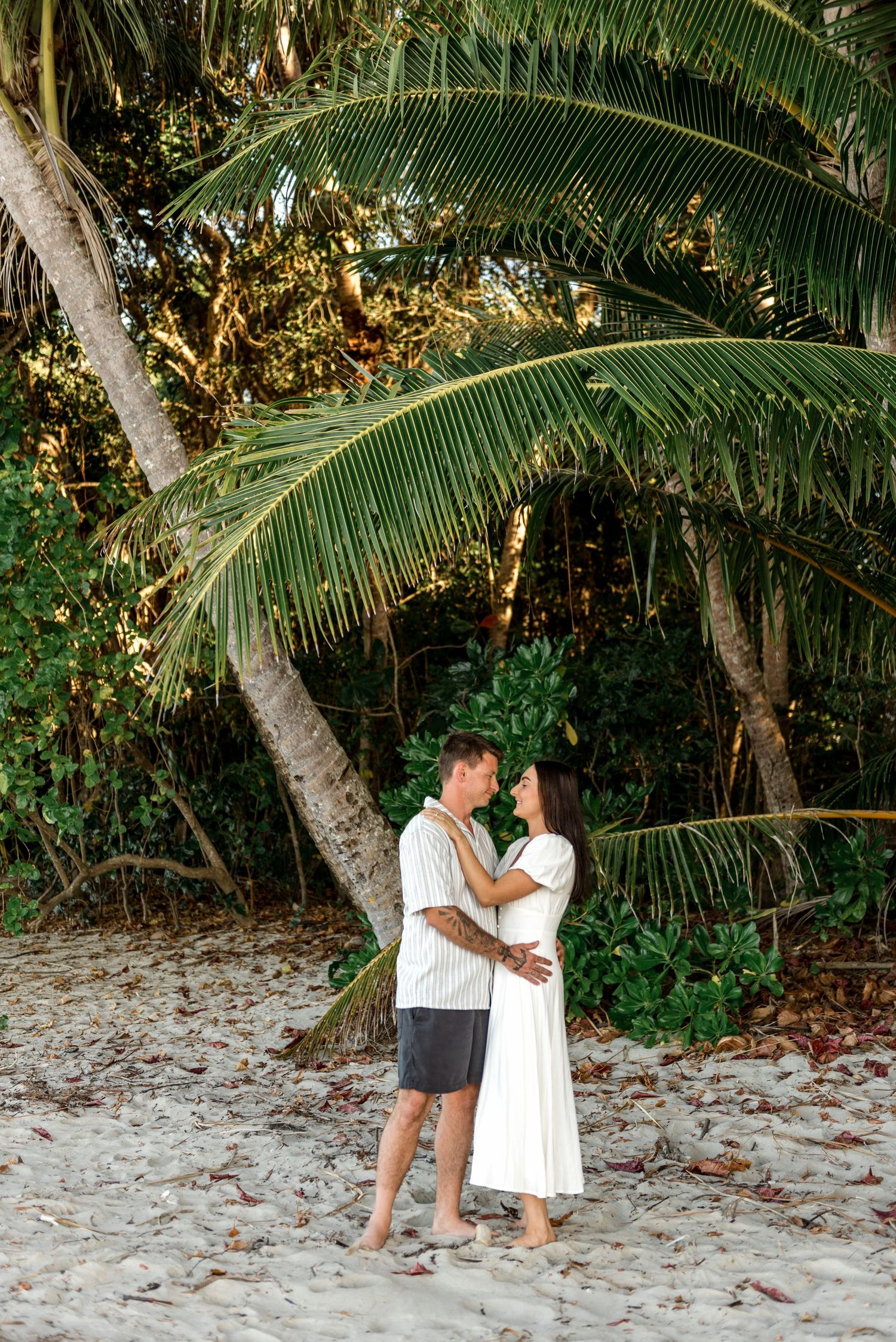 Couple embracing on a sandy beach surrounded by lush tropical palm trees.