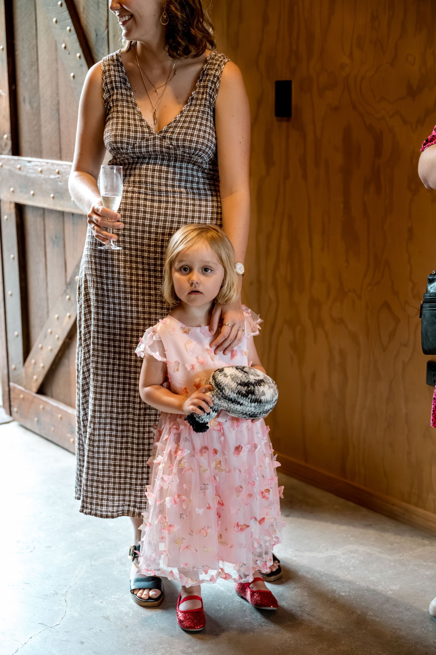 Young girl in pink dress holds a disco ball purse beside a pregnant woman at a wedding.