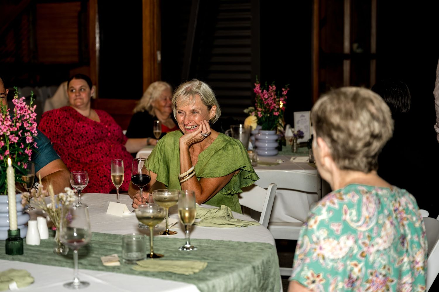 Woman in green dress smiling at a candlelit wedding reception dinner table.