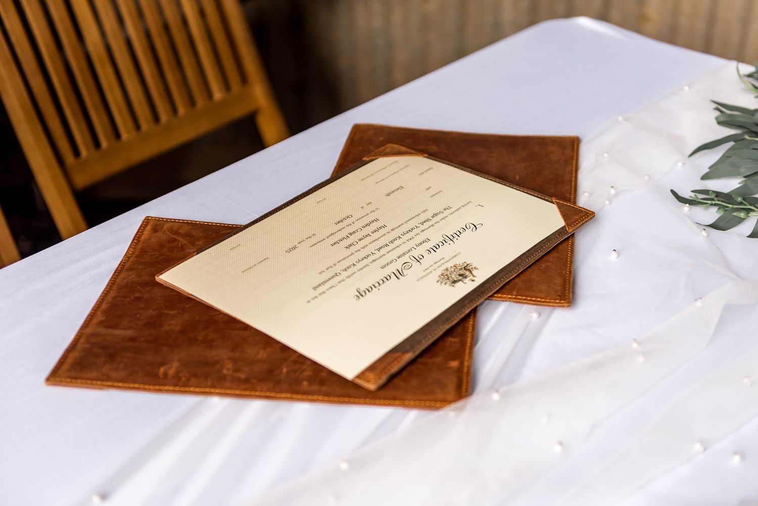 Leather-bound wedding ceremony programs stacked on a white linen covered table.
