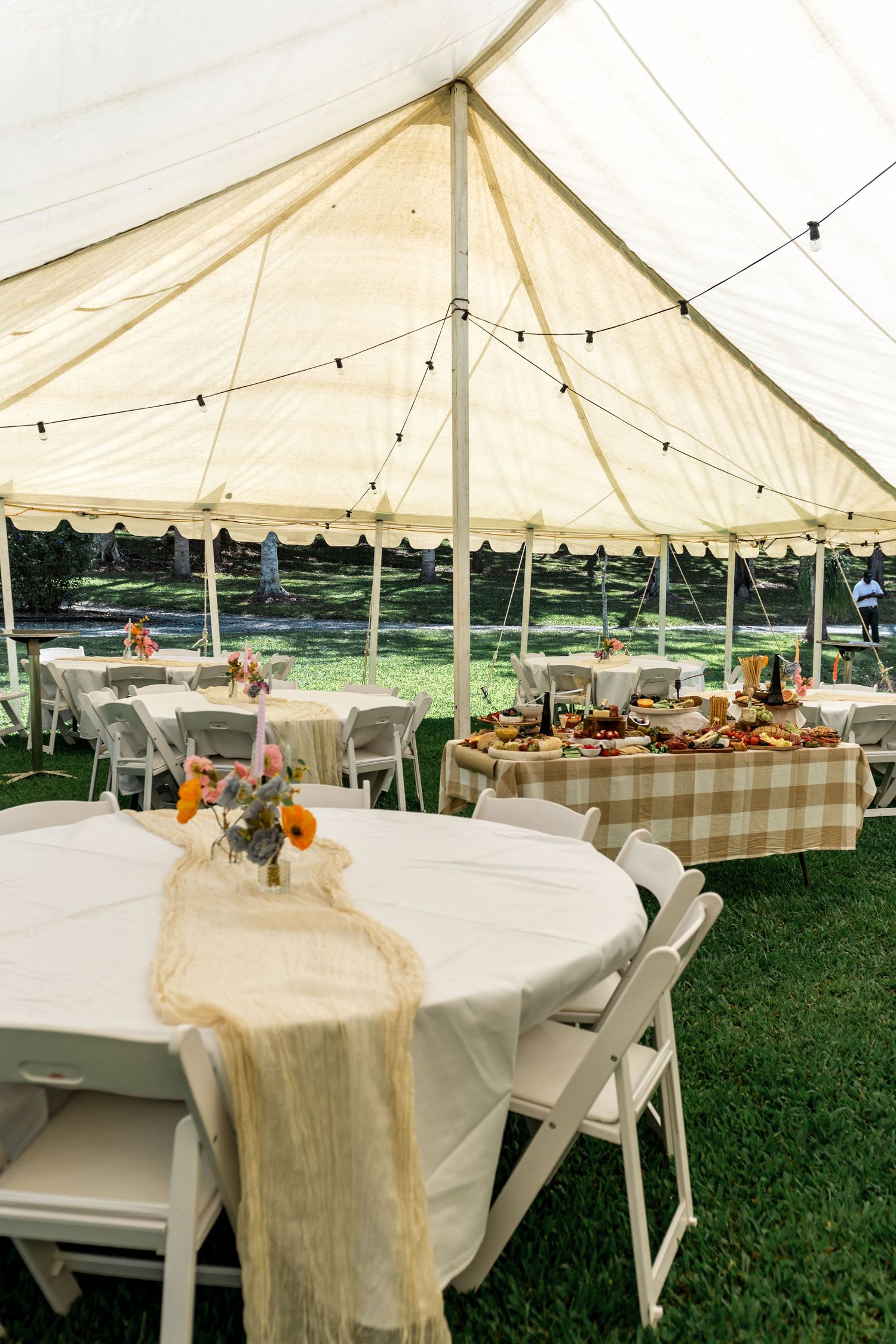 Elegant outdoor wedding reception tent with round tables, string lights, and a charcuterie spread.