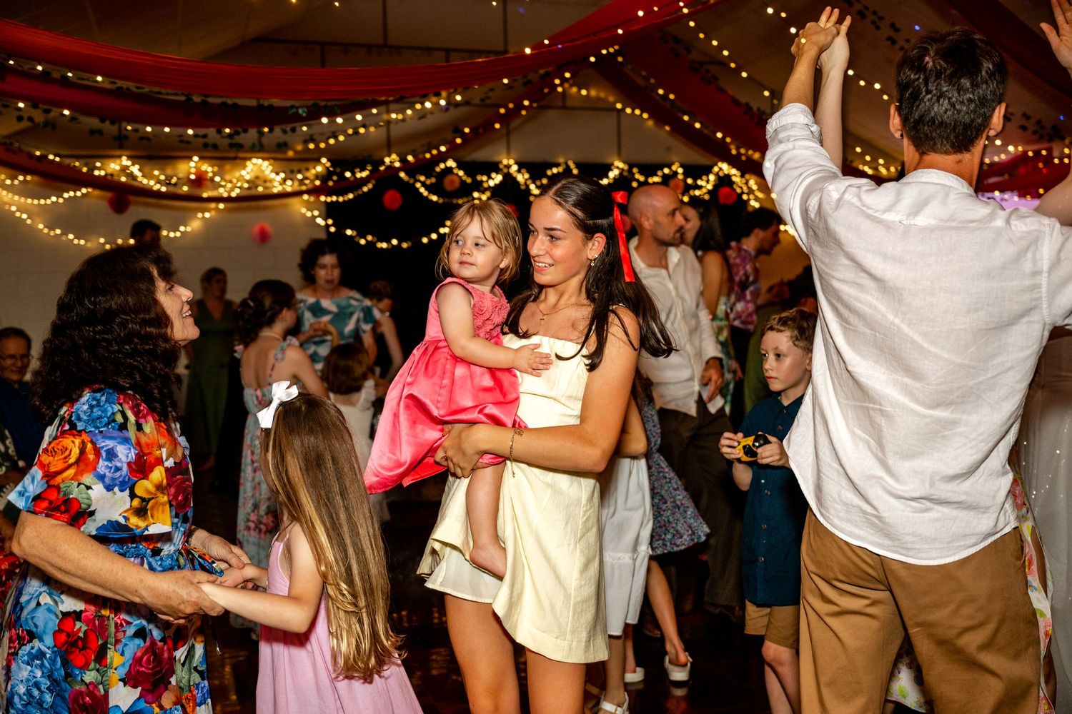 Woman holding a toddler in pink dress while dancing at wedding reception.