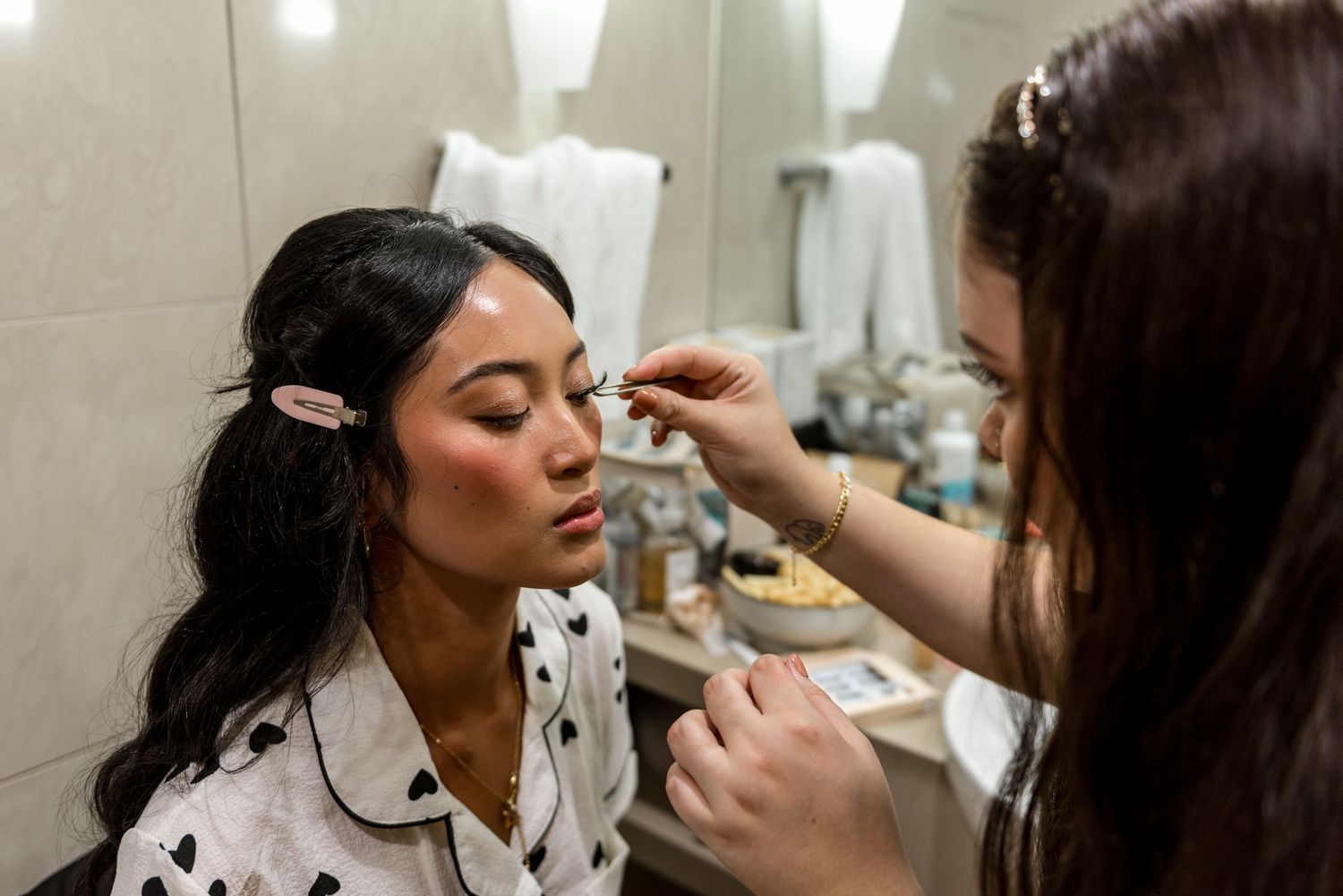 Makeup artist applying eyeshadow to a bride during wedding preparations in a bathroom mirror setting.