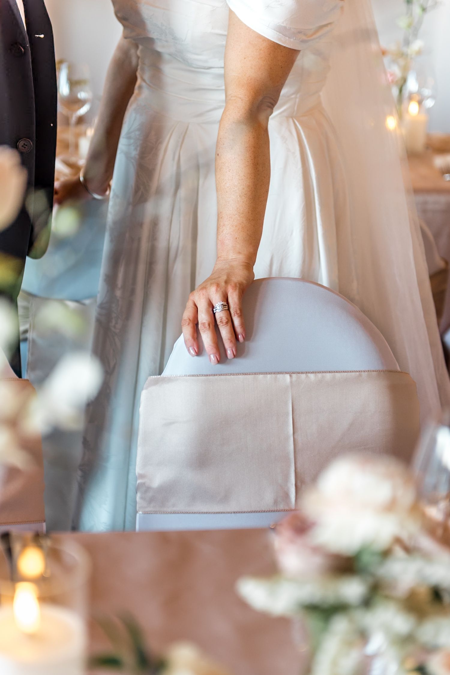 Close-up of bride's hand resting on chair back showcasing her diamond wedding ring at reception.