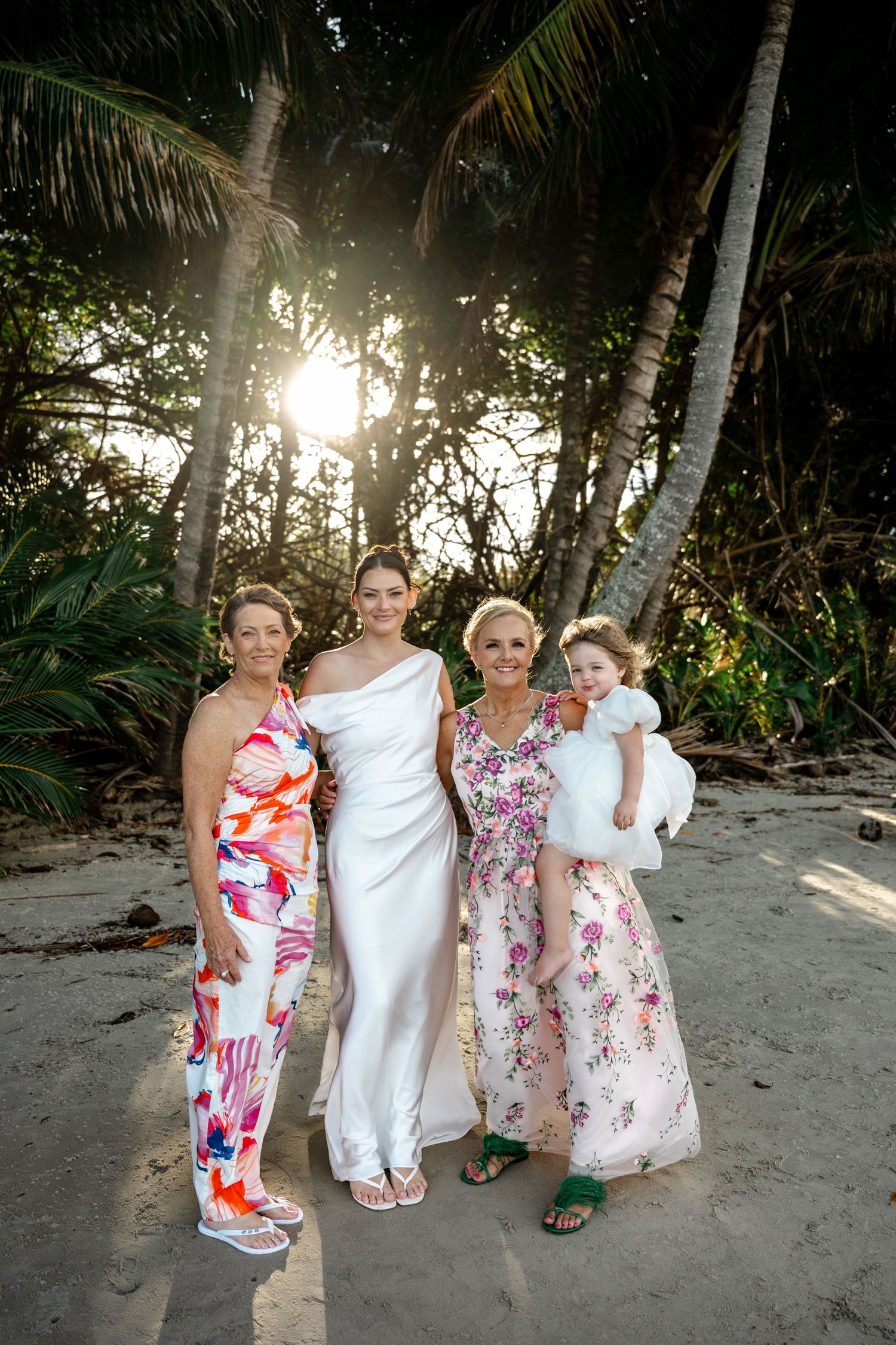 Bride in white gown poses with three female family members including a child on a tropical beach at Four Mile Beach, Port Douglas.