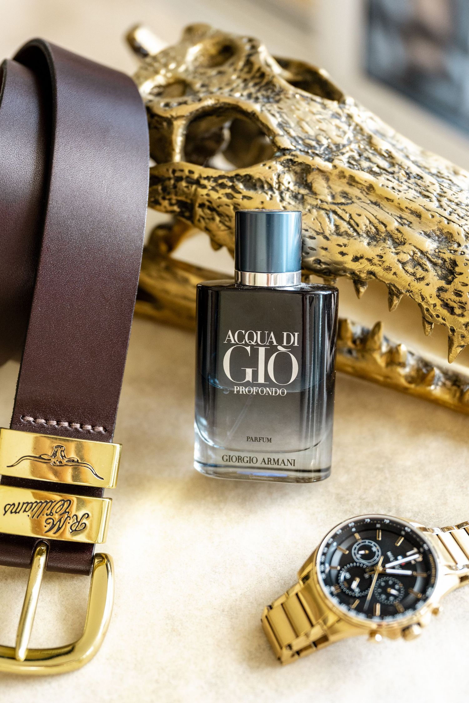 Giorgio Armani Acqua di Gio Profondo parfum bottle beside a brown leather belt and gold watch.