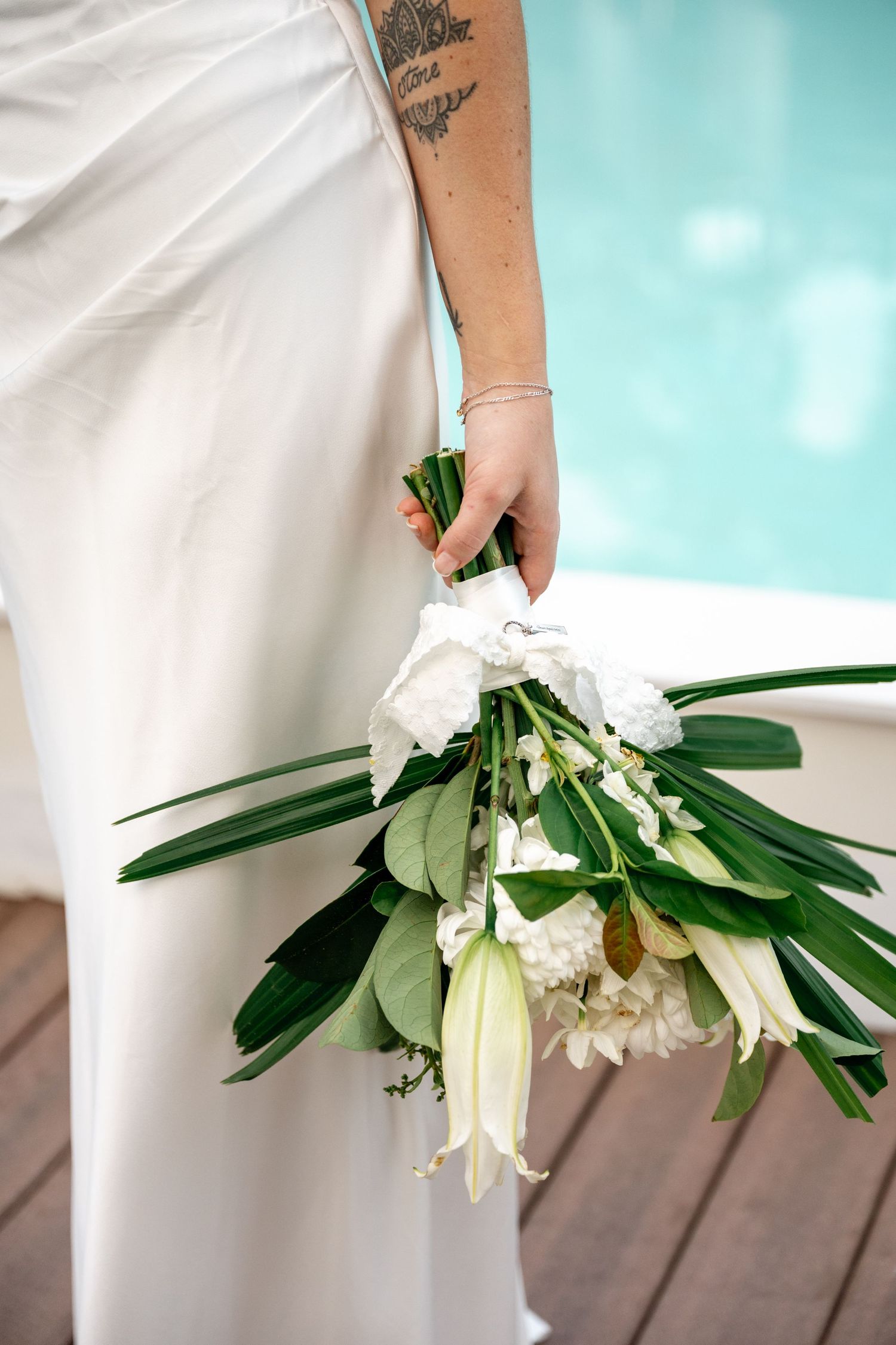 Bride holding a tropical white wedding bouquet with green leaves beside a turquoise pool at Sheraton Grand Mirage Port Douglas.