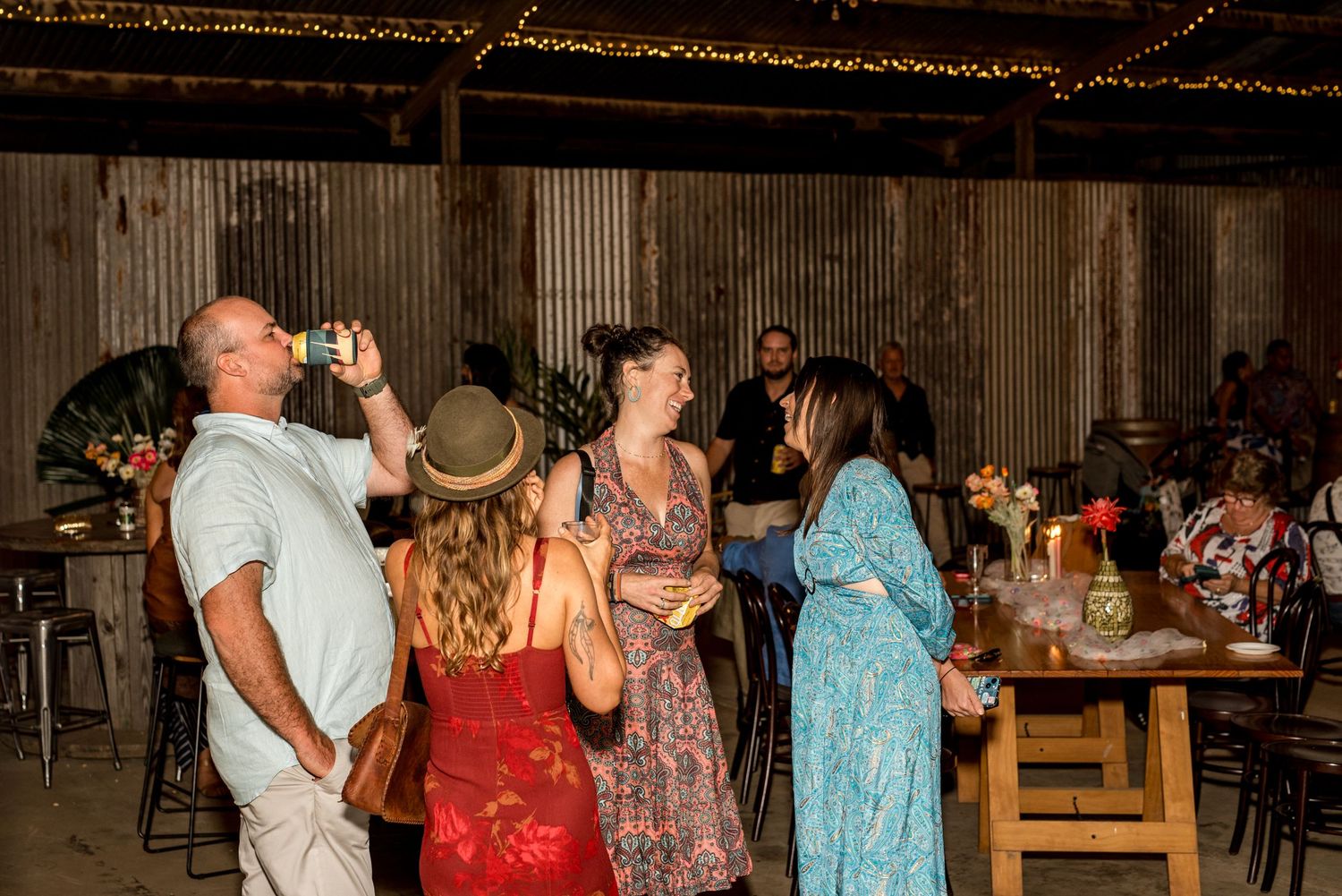 Guests socializing and drinking at The Sugar Shed rustic barn wedding reception with fairy lights.