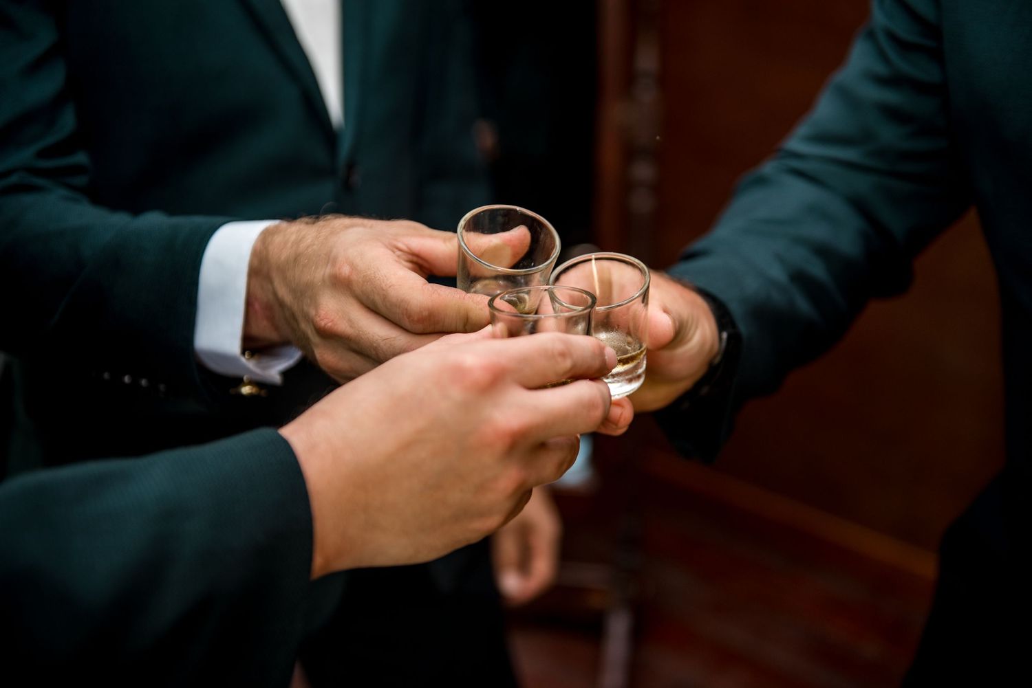 Groomsmen clinking shot glasses in a pre-wedding celebration toast.