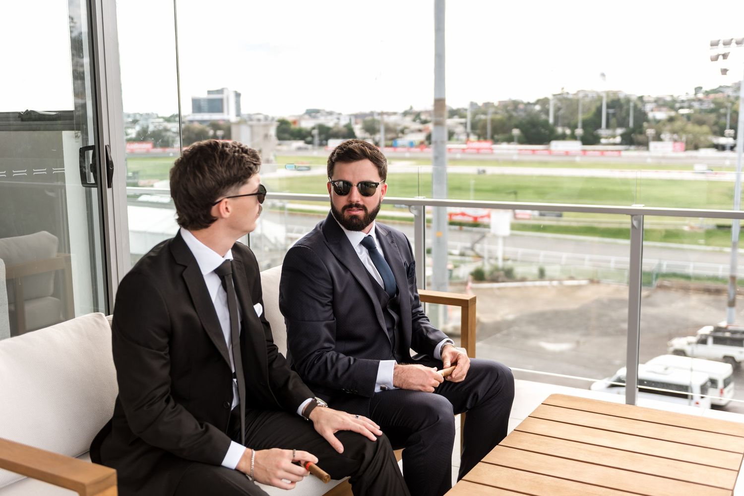 Two groomsmen in dark suits laughing and relaxing together before the wedding ceremony.