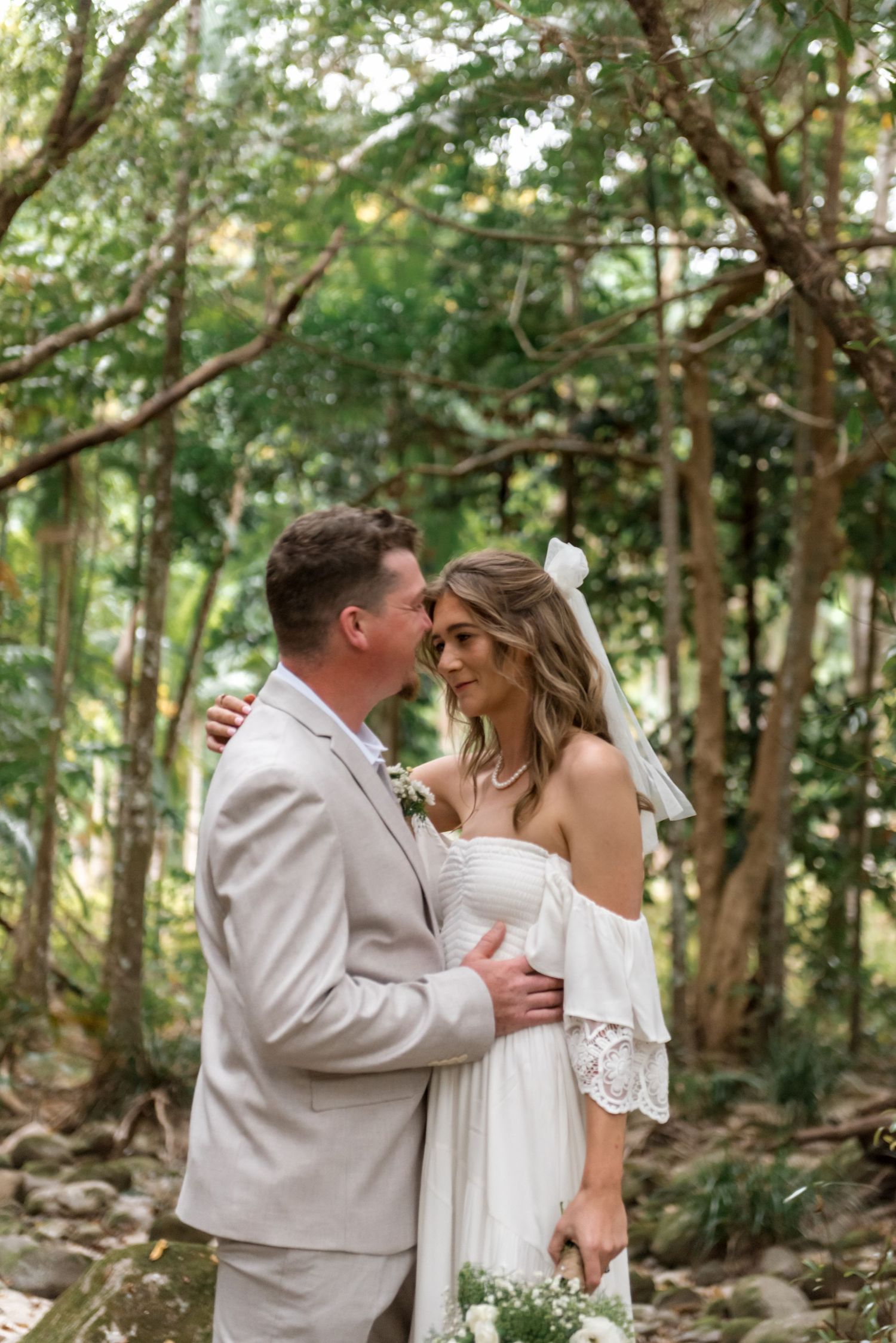 Bride and groom smiling at each other under a natural tree arch in forest.