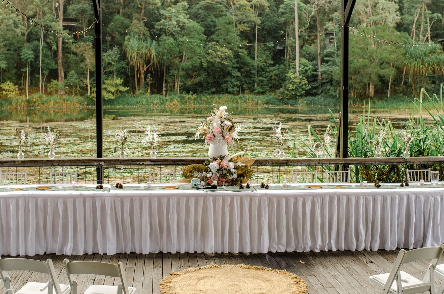 Elegant wedding reception head table with floral centerpiece overlooking a serene lily pond.