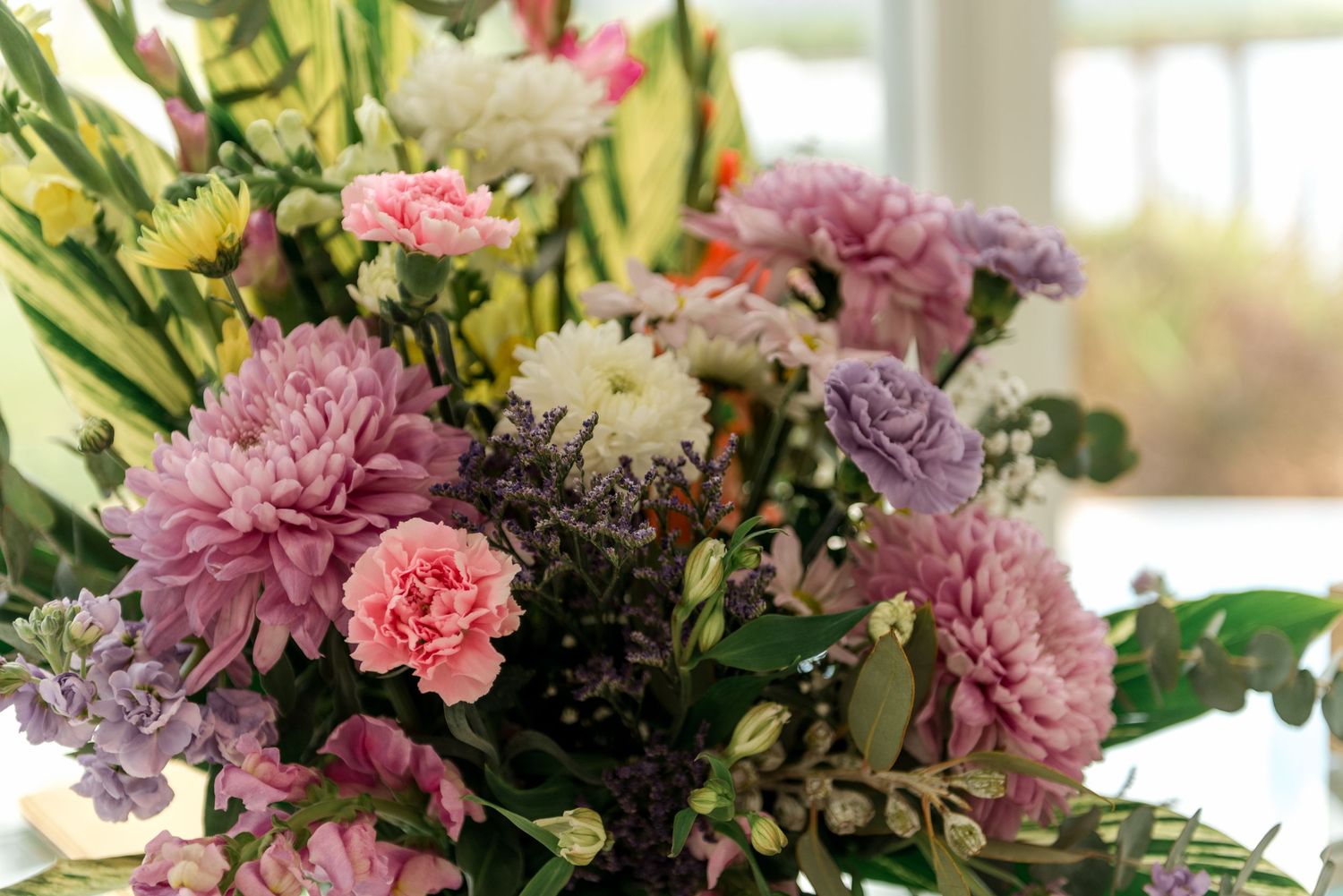 Elegant wedding floral centerpiece featuring pink chrysanthemums, carnations, and purple blooms.