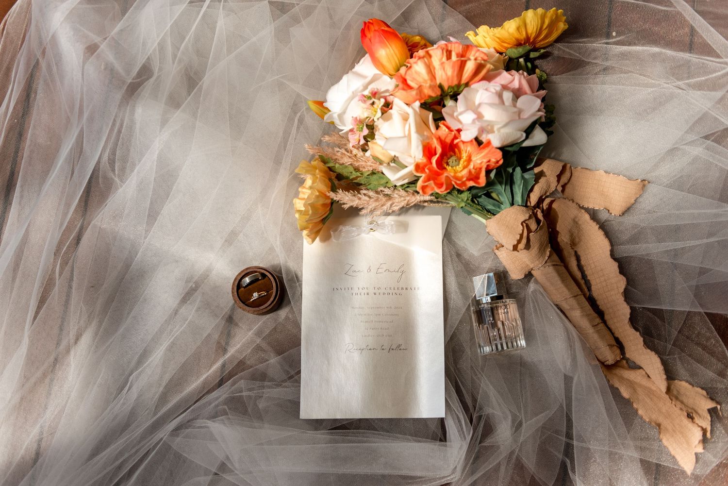 Flat lay of bridal bouquet, wedding invitation, perfume bottle and tulle veil.
