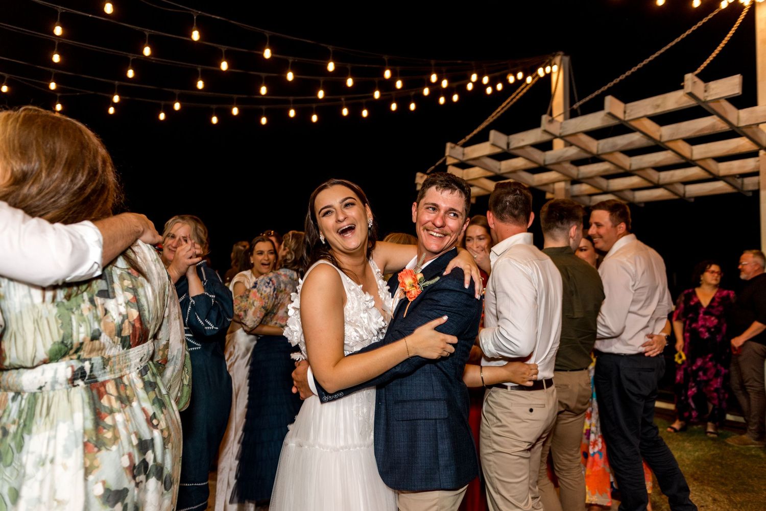 Bride and groom dancing joyfully under string lights at outdoor wedding reception.