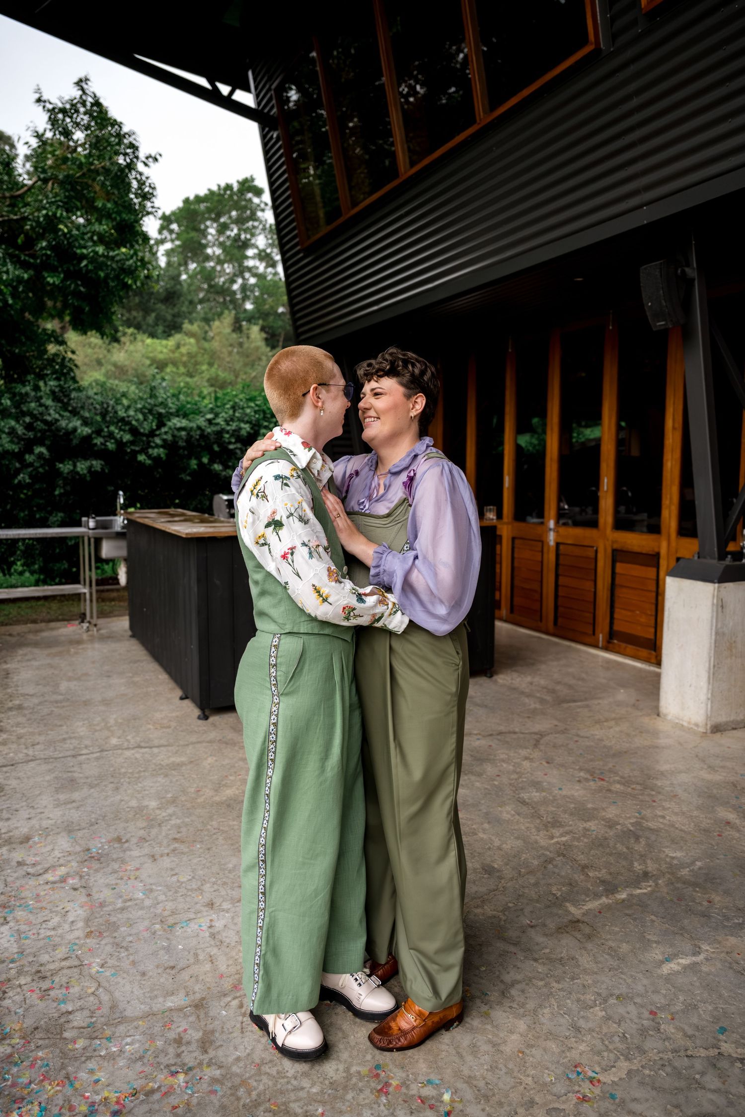 Two people in green outfits embracing and laughing on a covered outdoor venue patio.