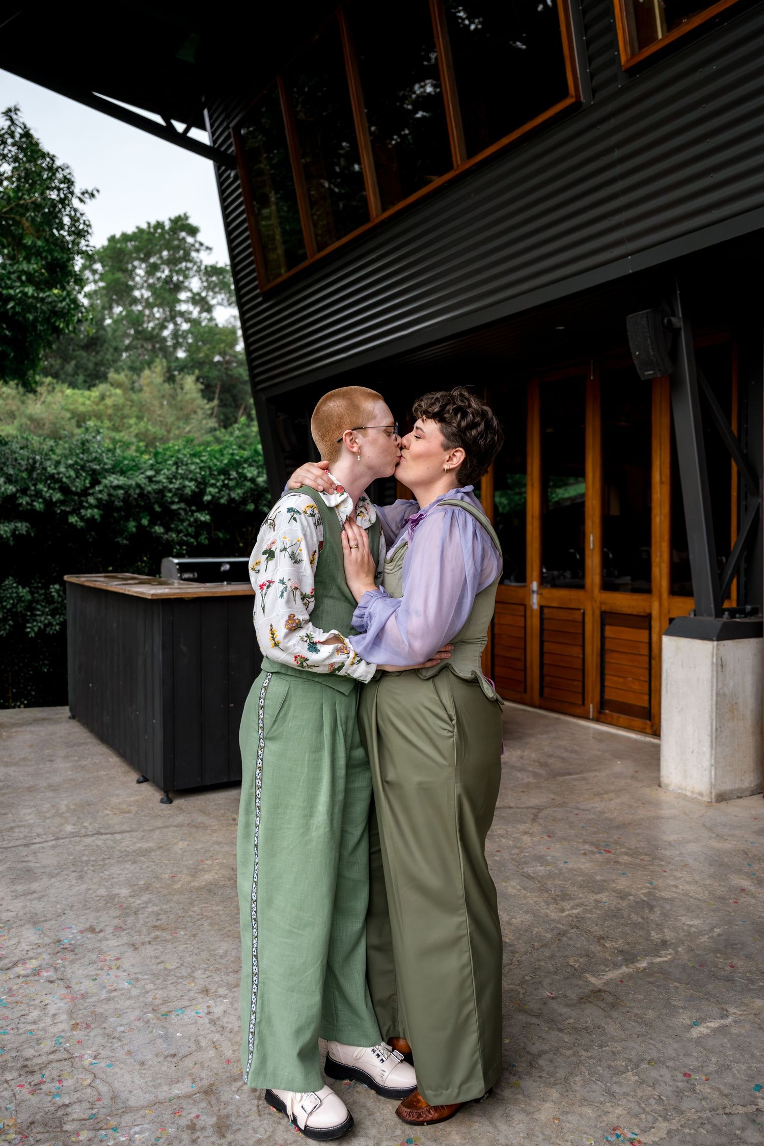 Couple in coordinated green outfits sharing a tender kiss on an outdoor venue patio.