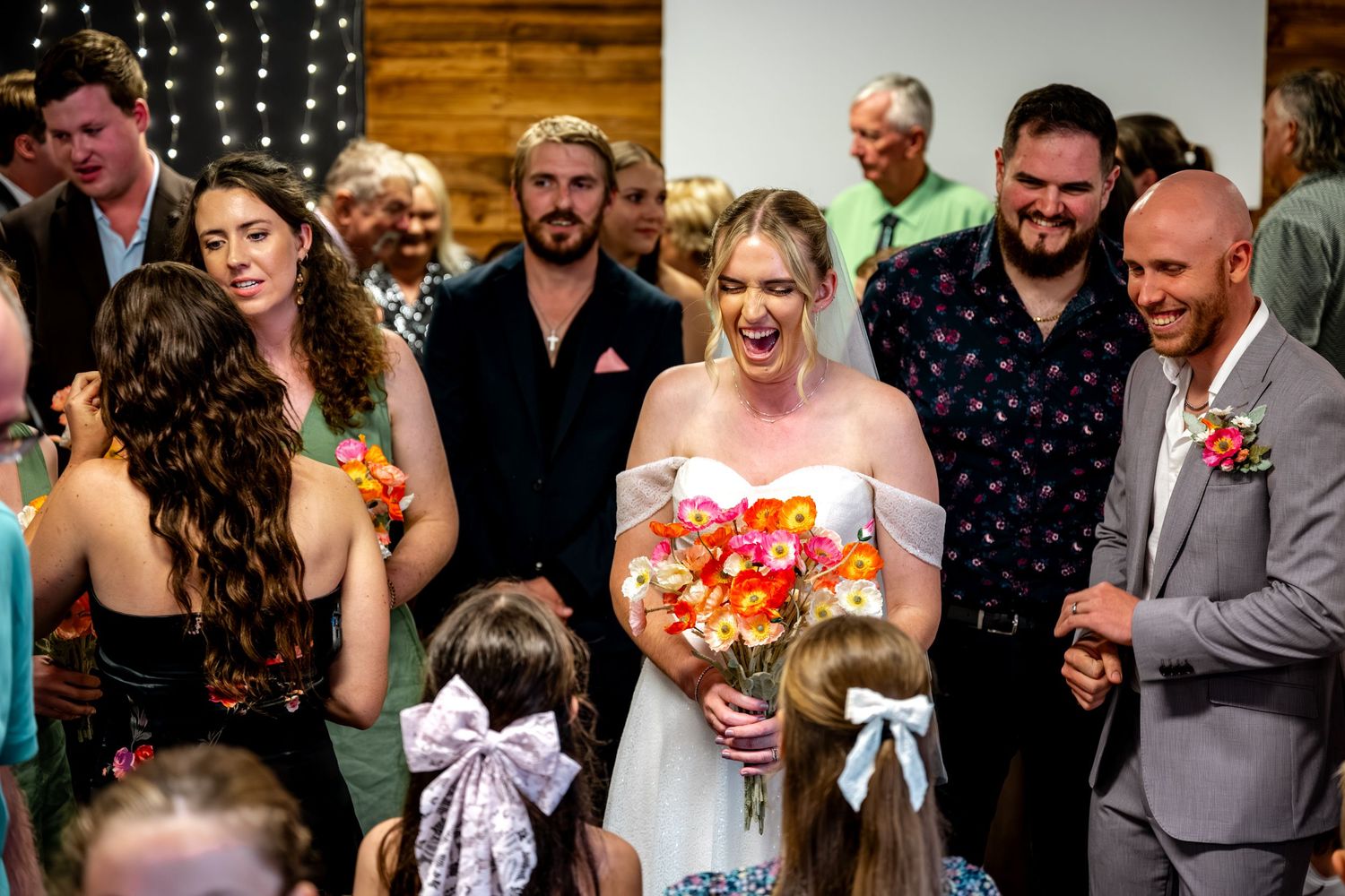 Laughing bride holds colorful bouquet while groom smiles during joyful wedding ceremony exit.
