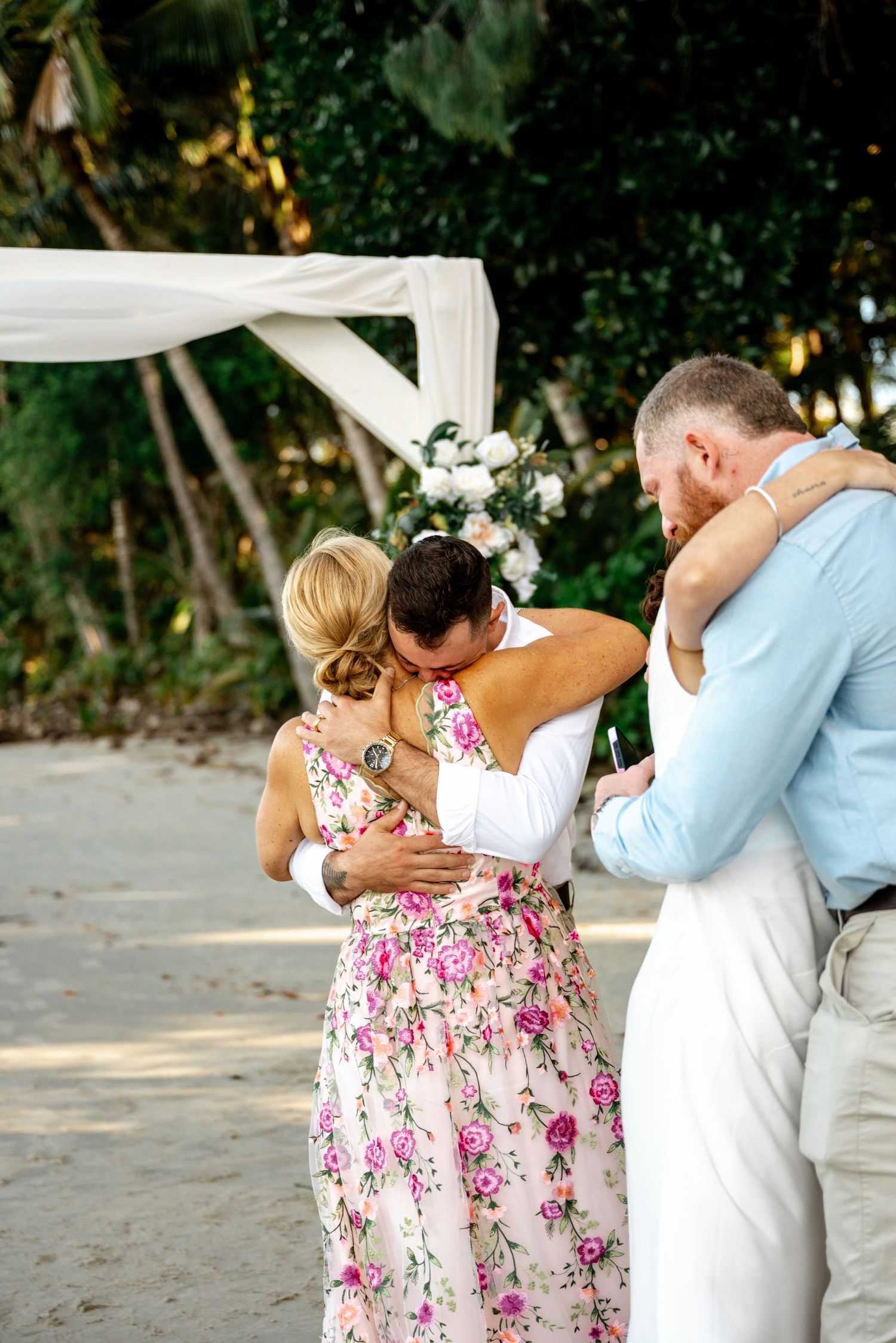 Couple embracing family members during an outdoor beach wedding ceremony under a white floral arch at Four Mile Beach, Port Douglas.