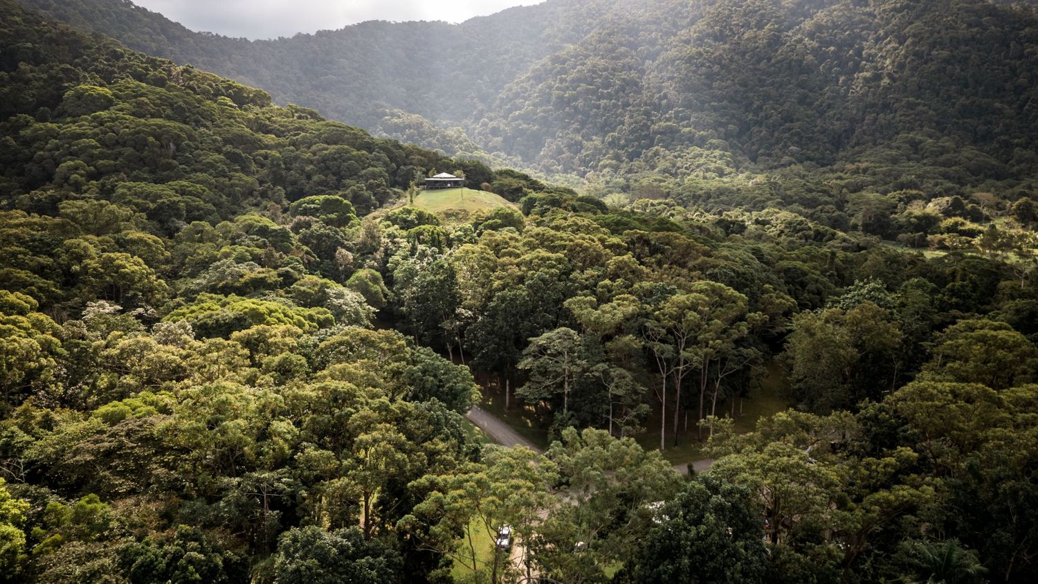 Breathtaking aerial view of a lush green mountain valley with a hidden wedding venue among the trees.